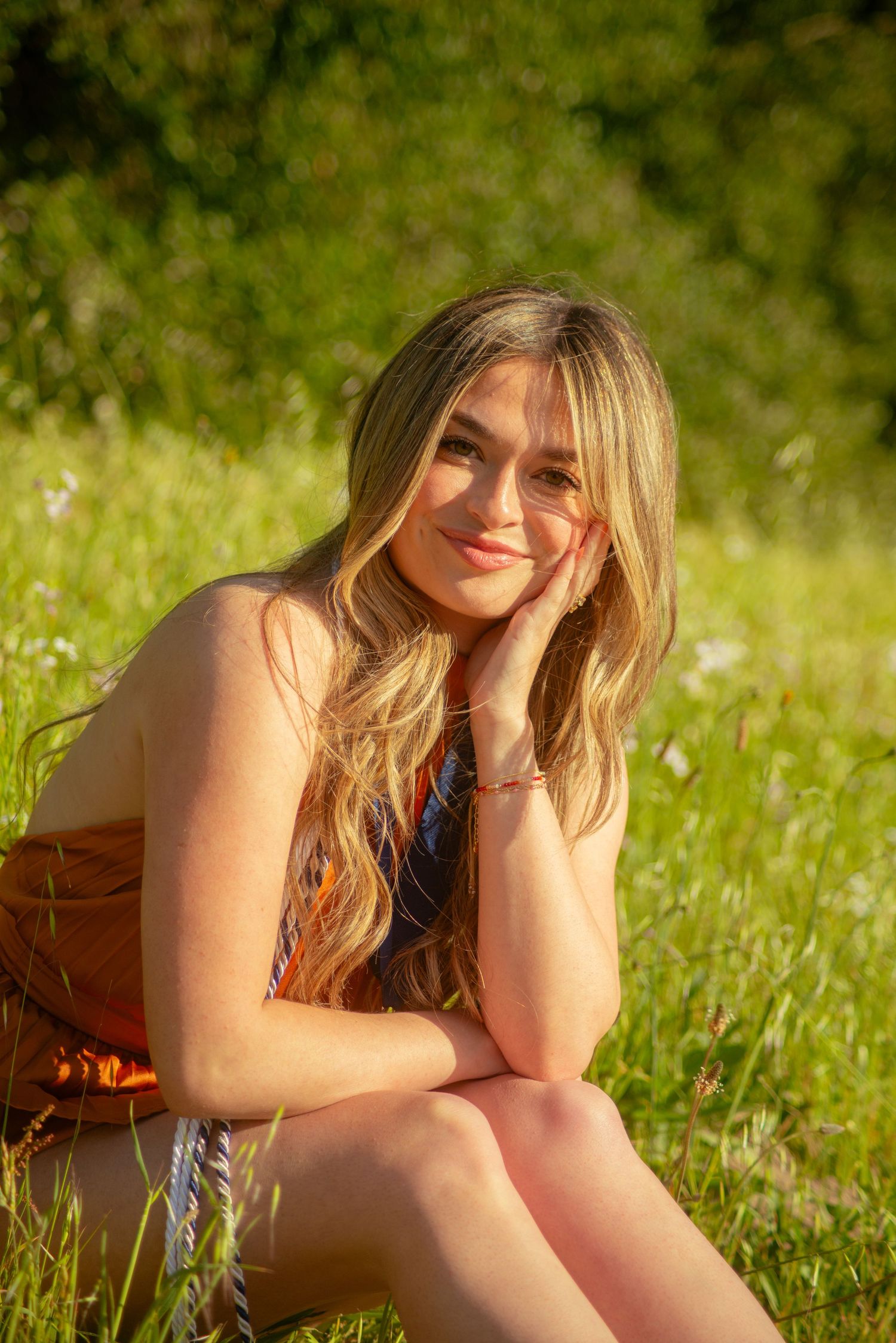 A person in a rust-colored dress reclines in a sunny wildflower field during golden hour.