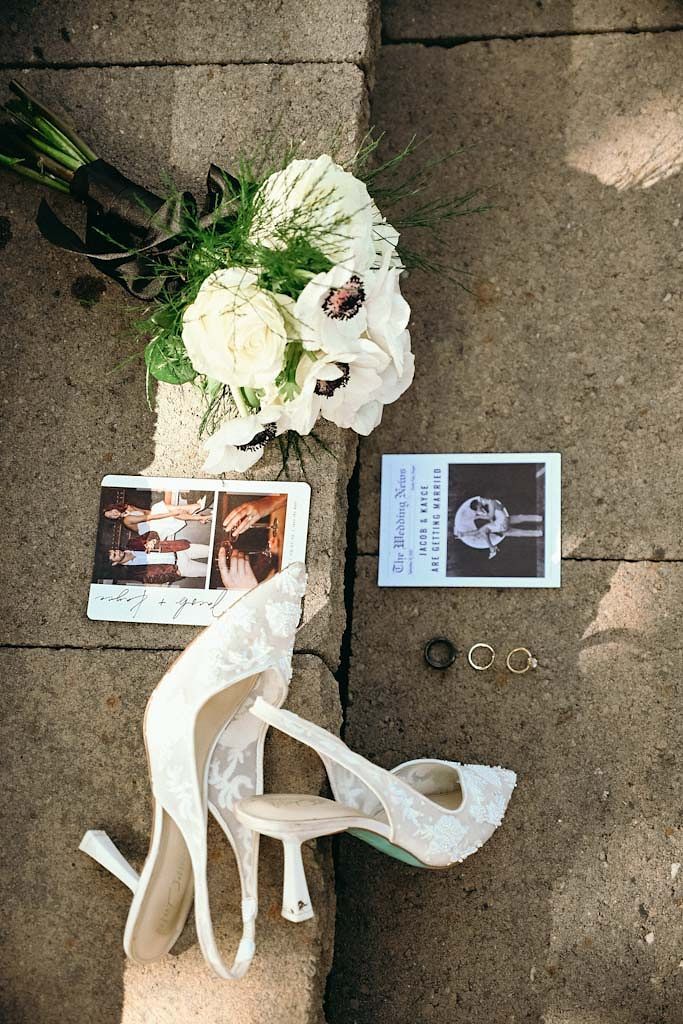 Wedding details flatlay with white shoes, flowers, rings and photo cards on concrete.