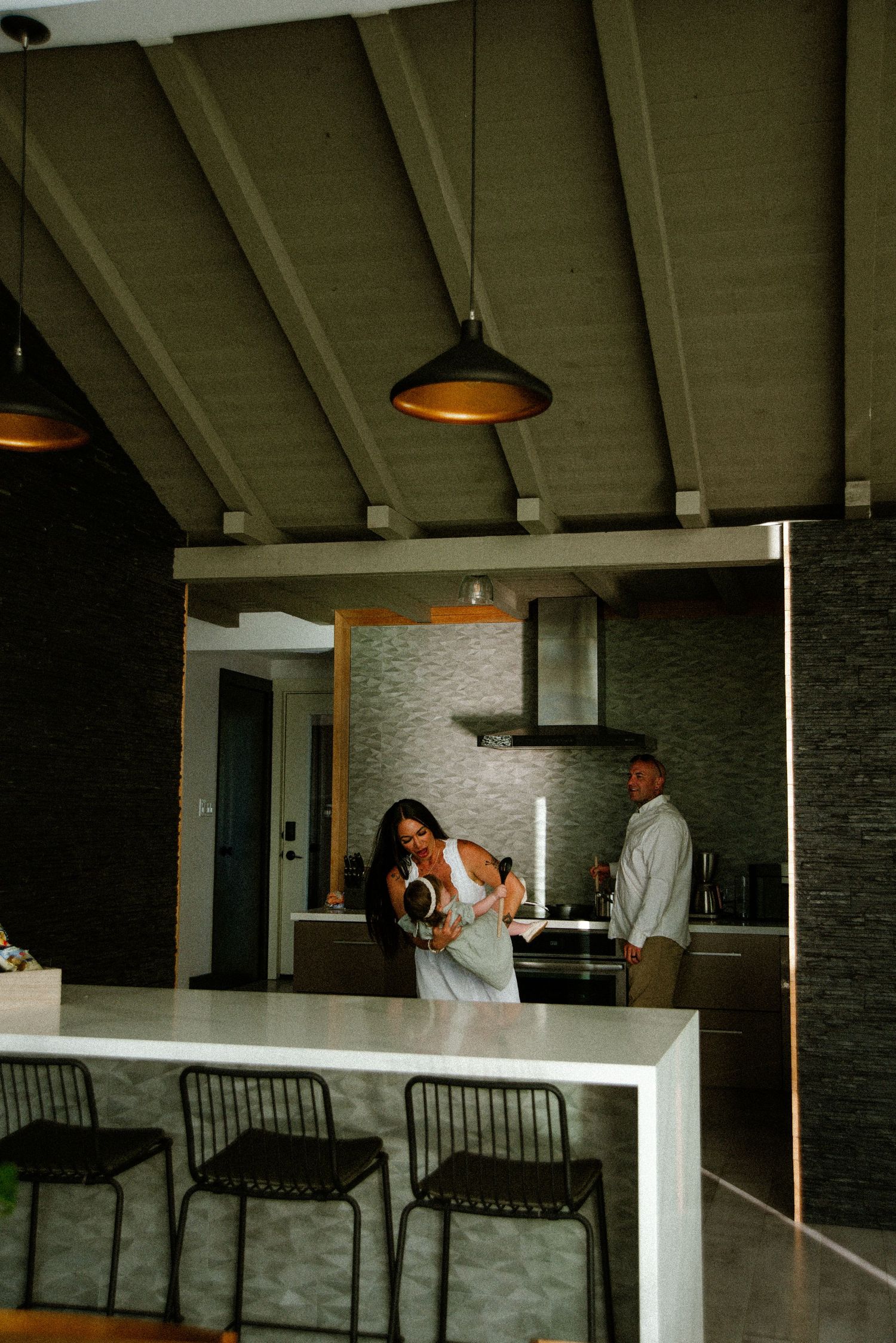 Modern kitchen interior with pendant lights and white counters showing two people interacting.