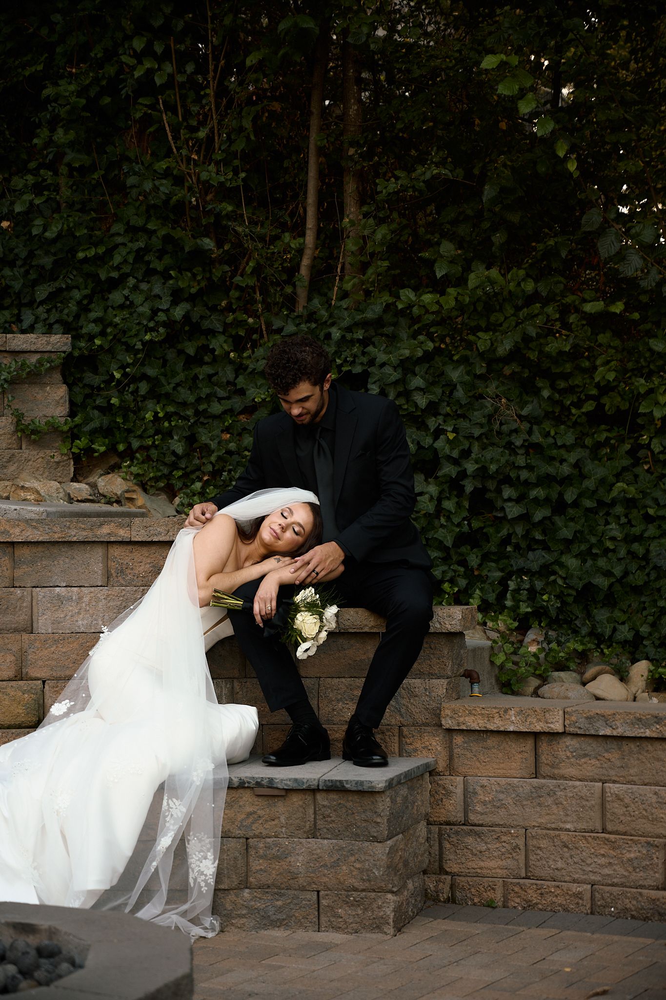 Couple shares intimate moment on stone steps surrounded by ivy at dusk.