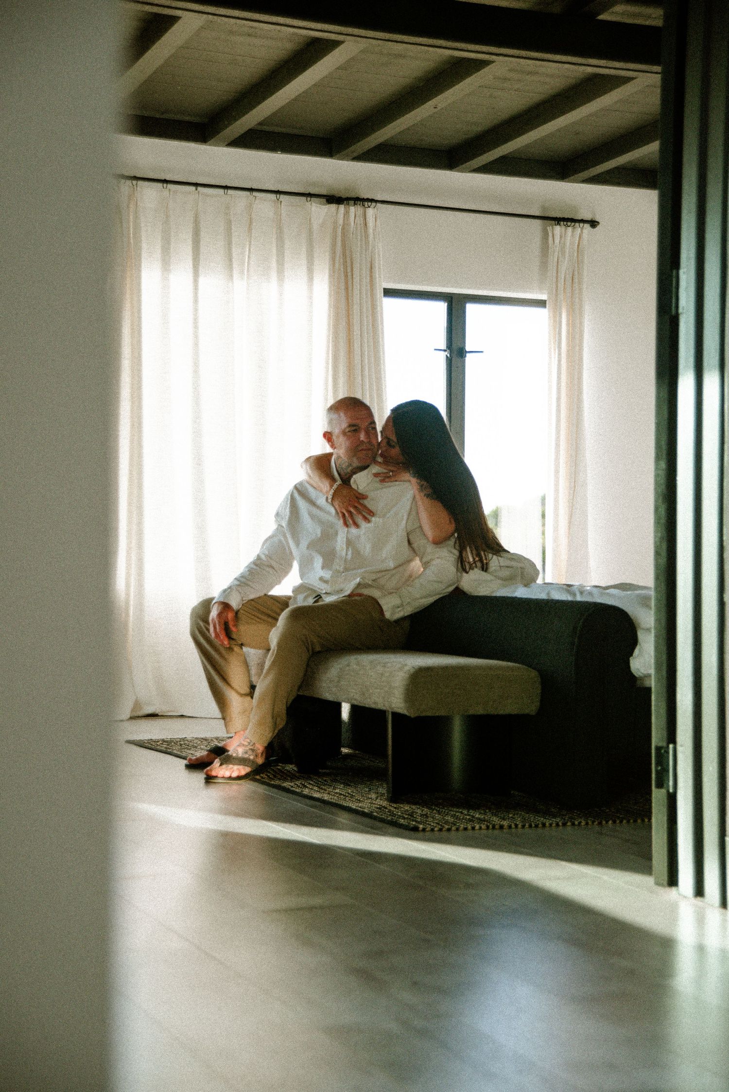 Couple relaxes together on minimalist white couch near window.