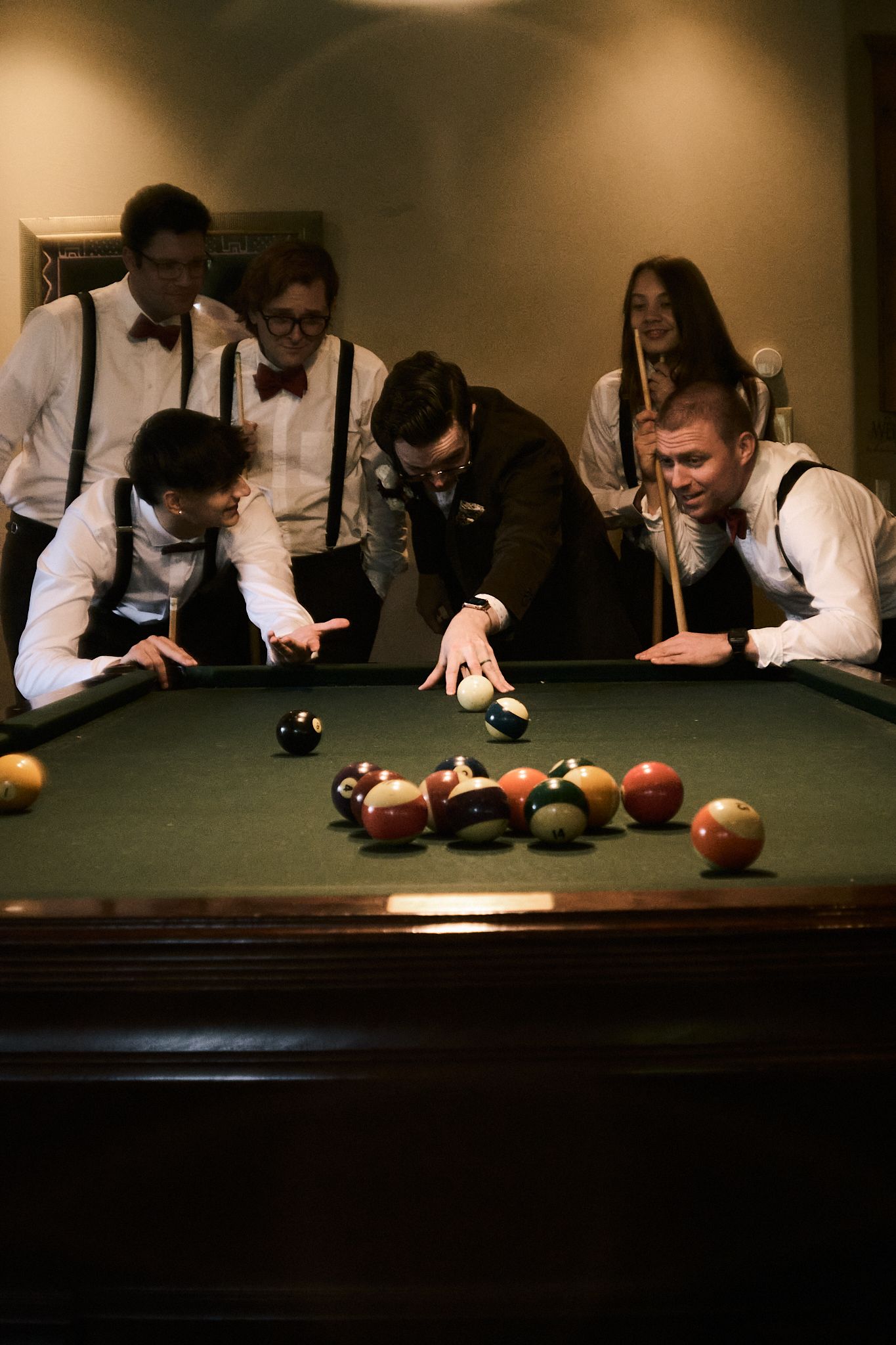 Group of men in suspenders playing pool billiards together at a green felt table during a formal gathering.