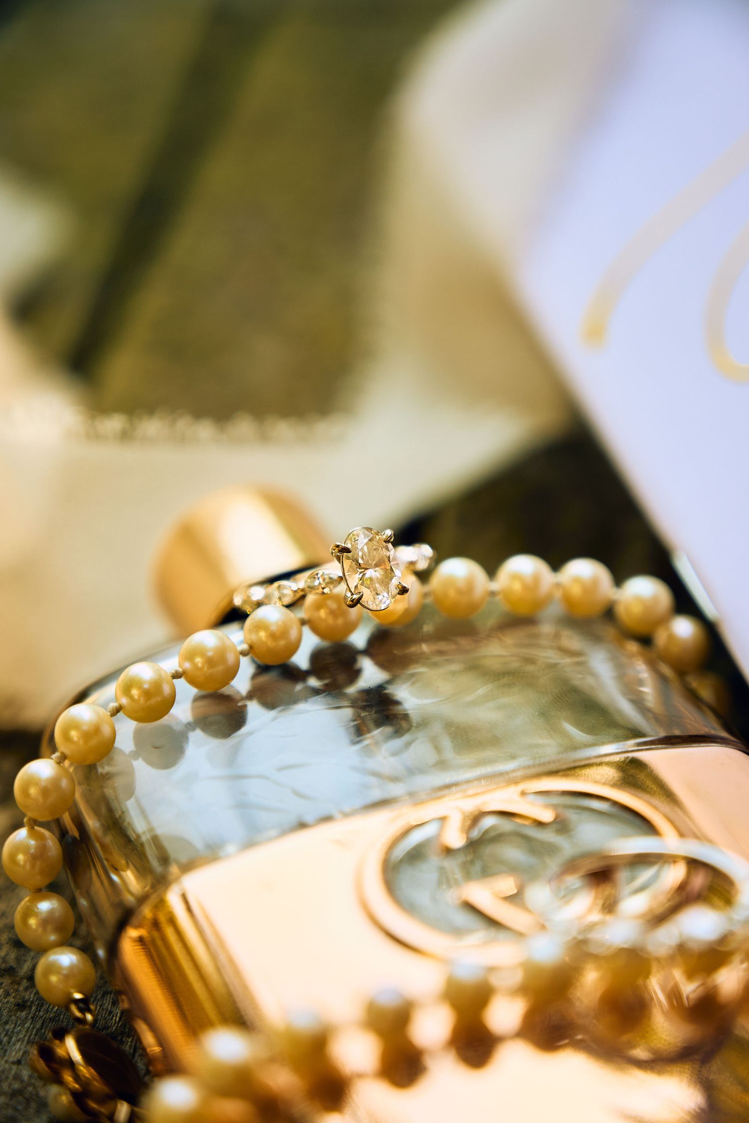Close-up of an elegant pearl bracelet and diamond ring resting on a gold Gucci perfume bottle.