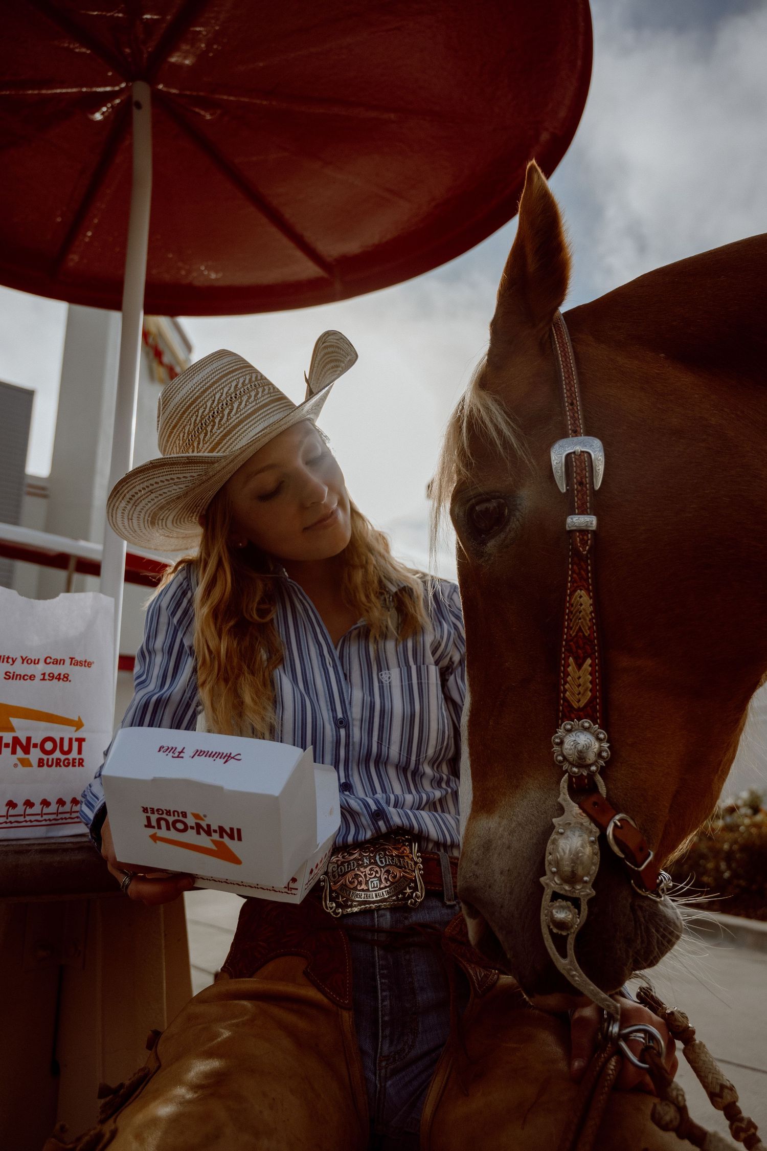 Person in western attire with horse at In-N-Out drive-through under red awning.