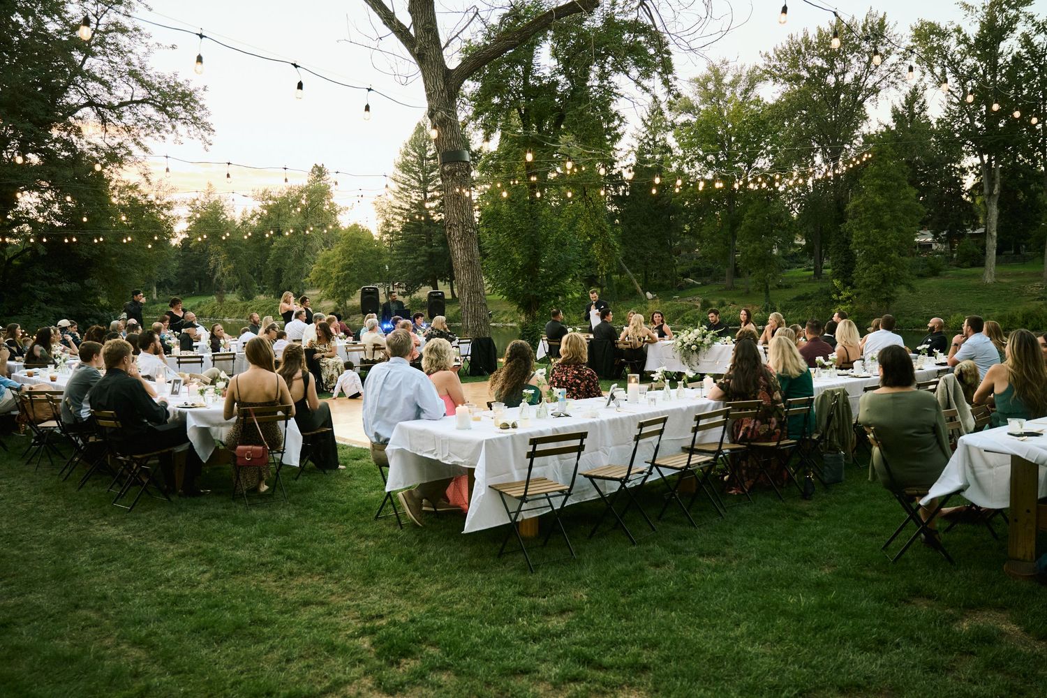 Guests enjoy an elegant outdoor wedding reception dinner under string lights at golden hour.