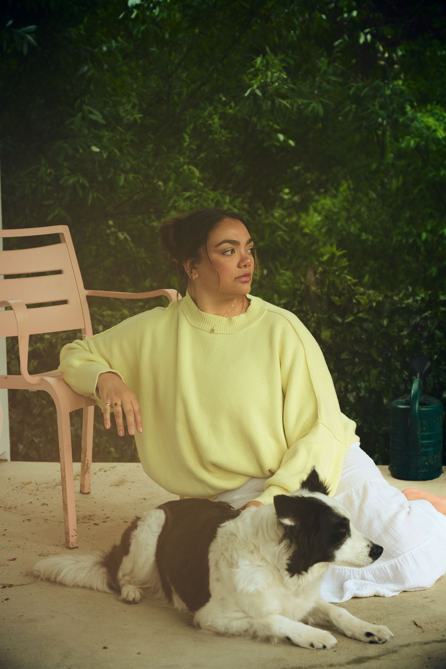 Woman in yellow sweatshirt sitting on patio with black and white dog beside her.