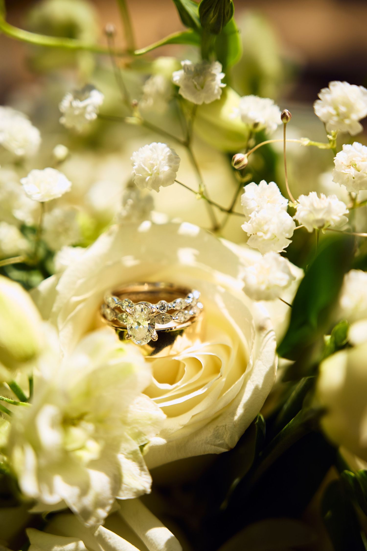 Gold diamond engagement ring and wedding band nestled inside a white rose in a bridal bouquet.