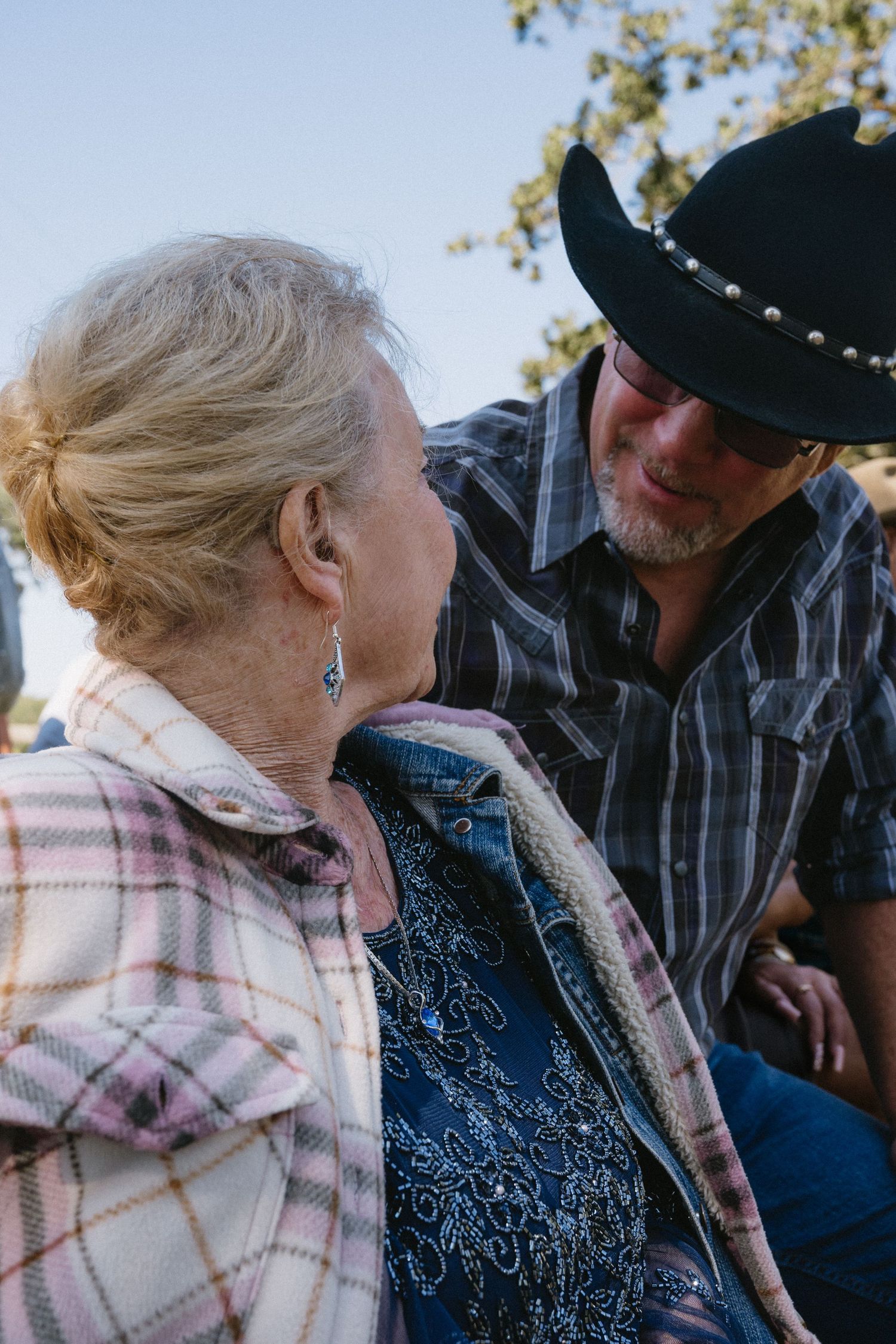Elderly woman and man in black cowboy hat share a warm conversation outdoors on a sunny day.