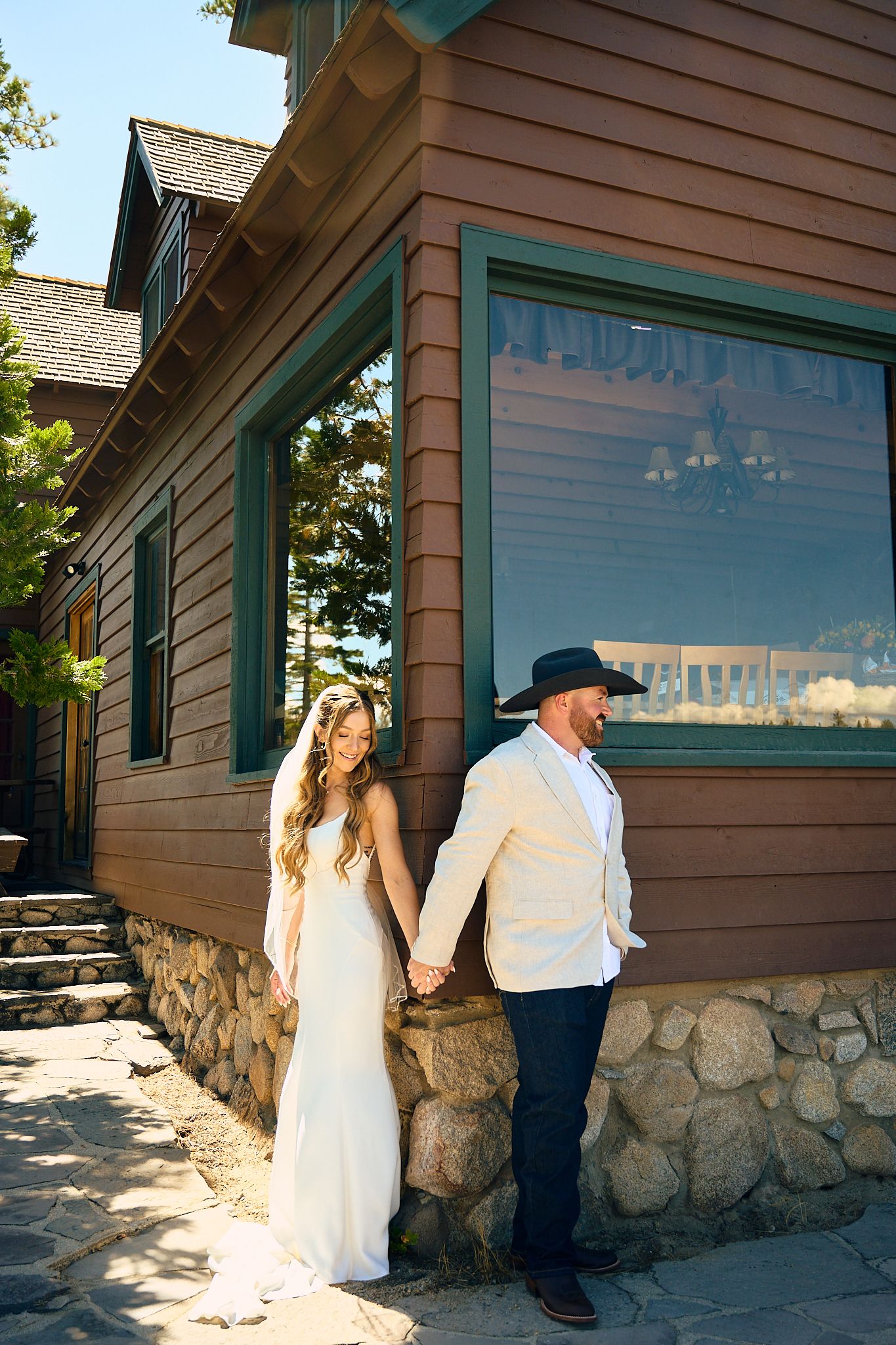 Bride and groom hold hands outside a rustic stone and wood building on their wedding day.