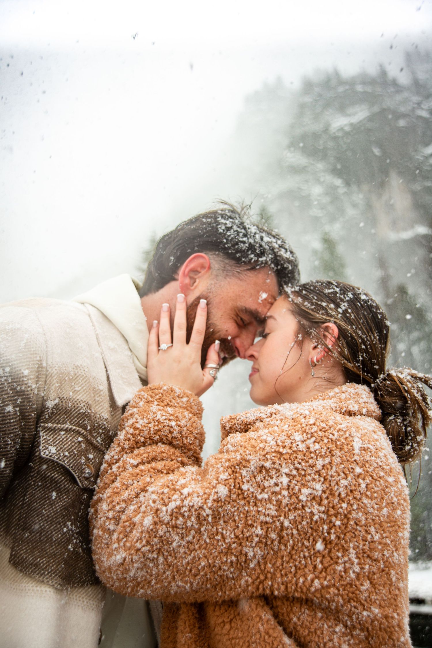 Snowflakes fall around a couple sharing a tender moment in winter weather.