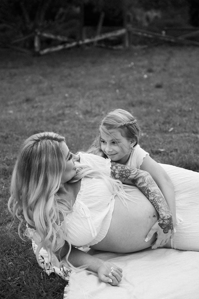 A tender black and white moment between a pregnant woman and child on a white blanket.