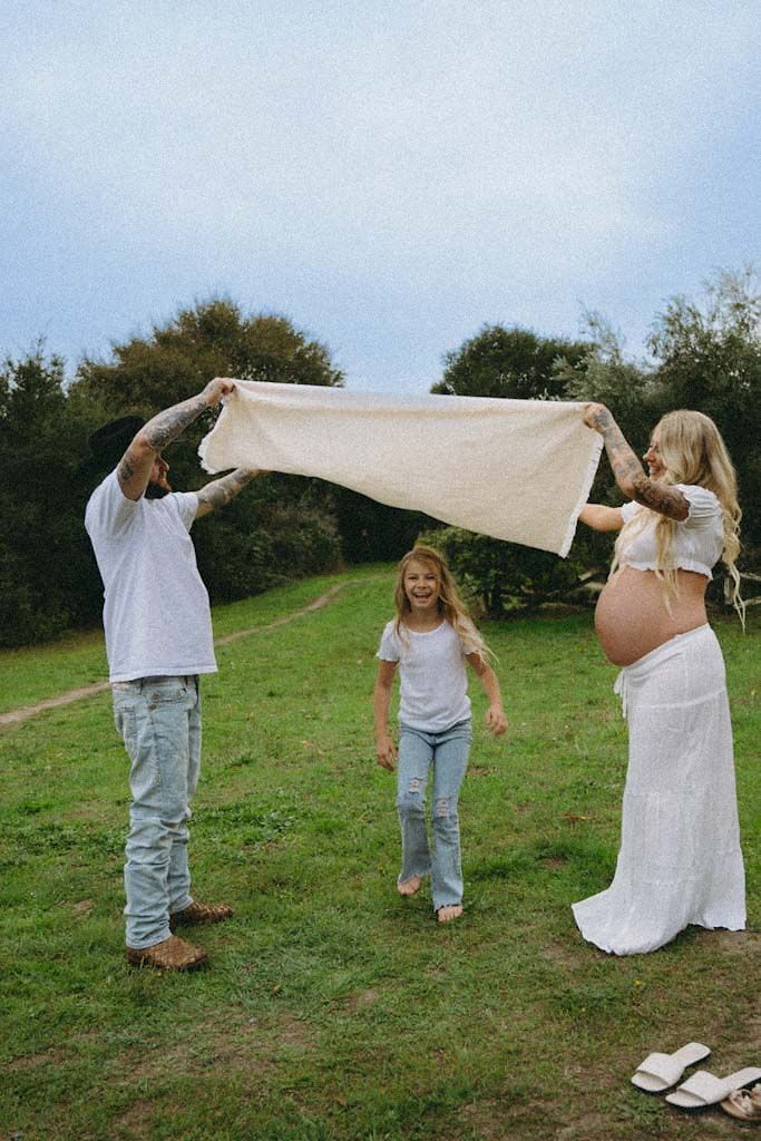 A family holds up a white sheet while playing together in a grassy field.