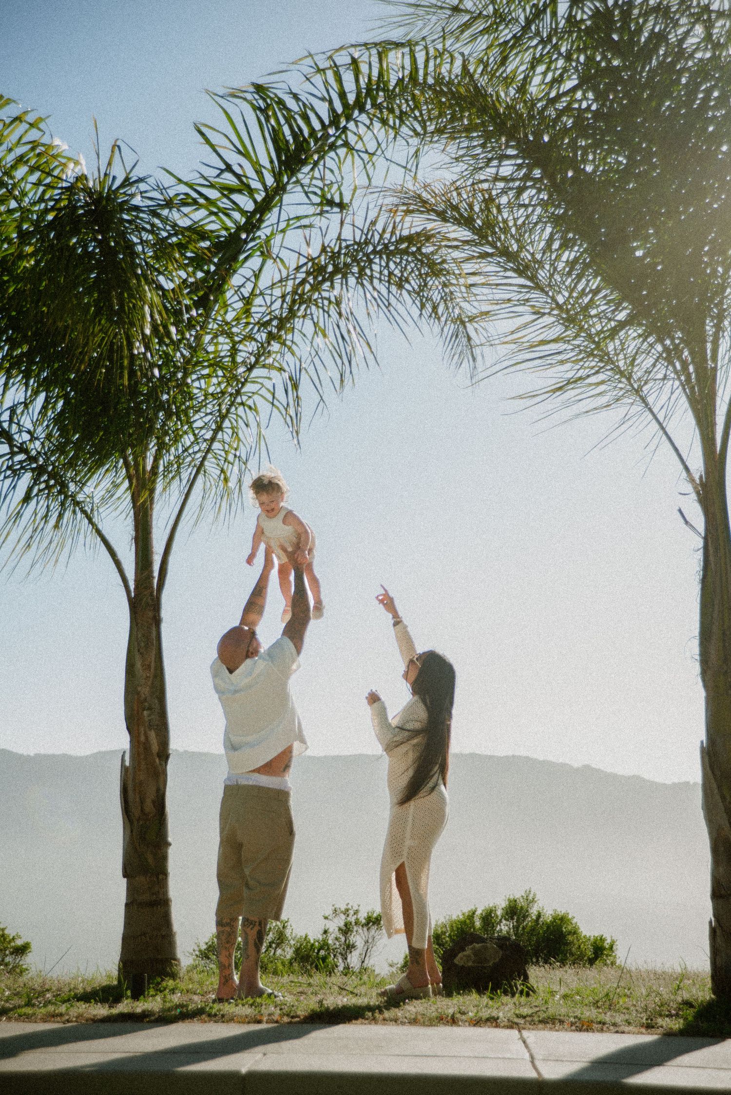 People play and interact by a pool with palm trees and mountains in the background.
