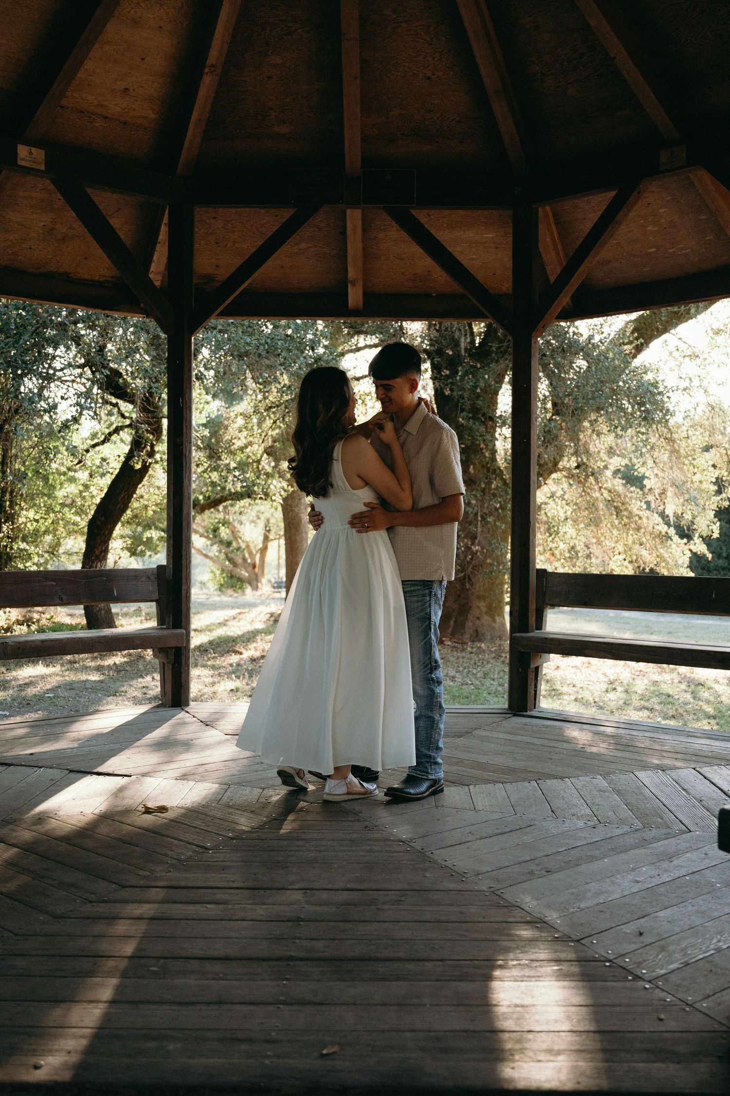 Couple dancing in a wooden gazebo during sunset.