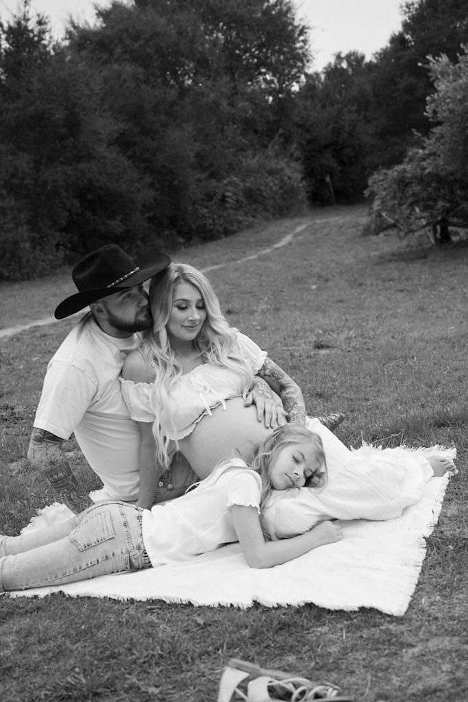 A family relaxes together on a blanket in a grassy field, captured in black and white.
