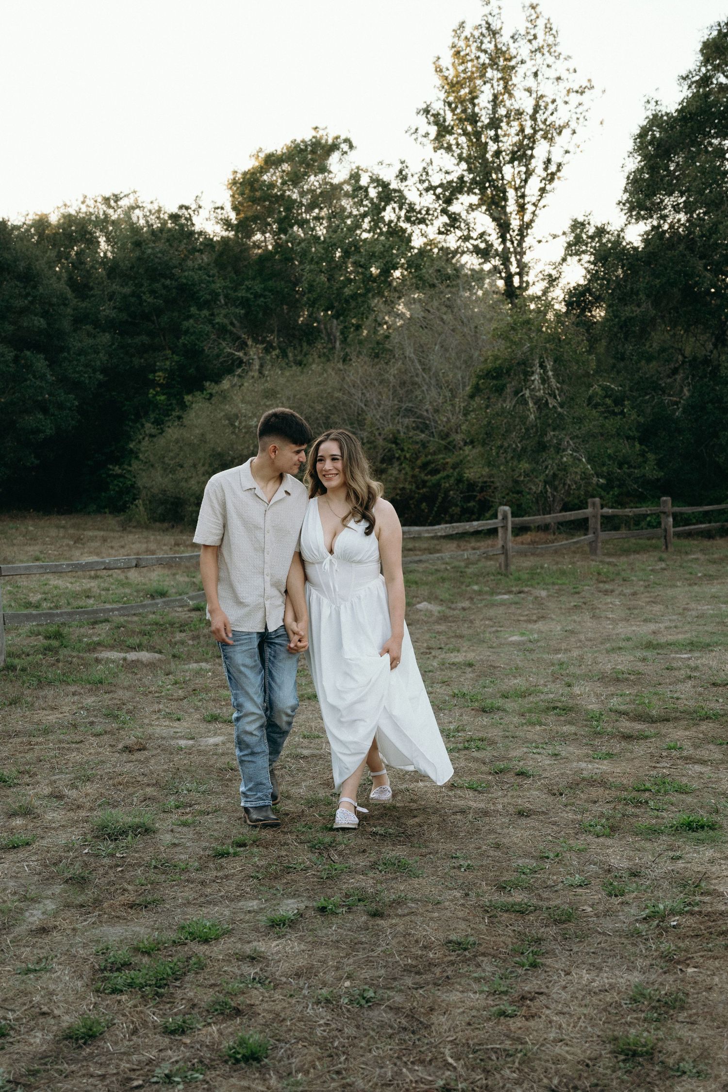 A couple walking together through a rustic field at golden hour.