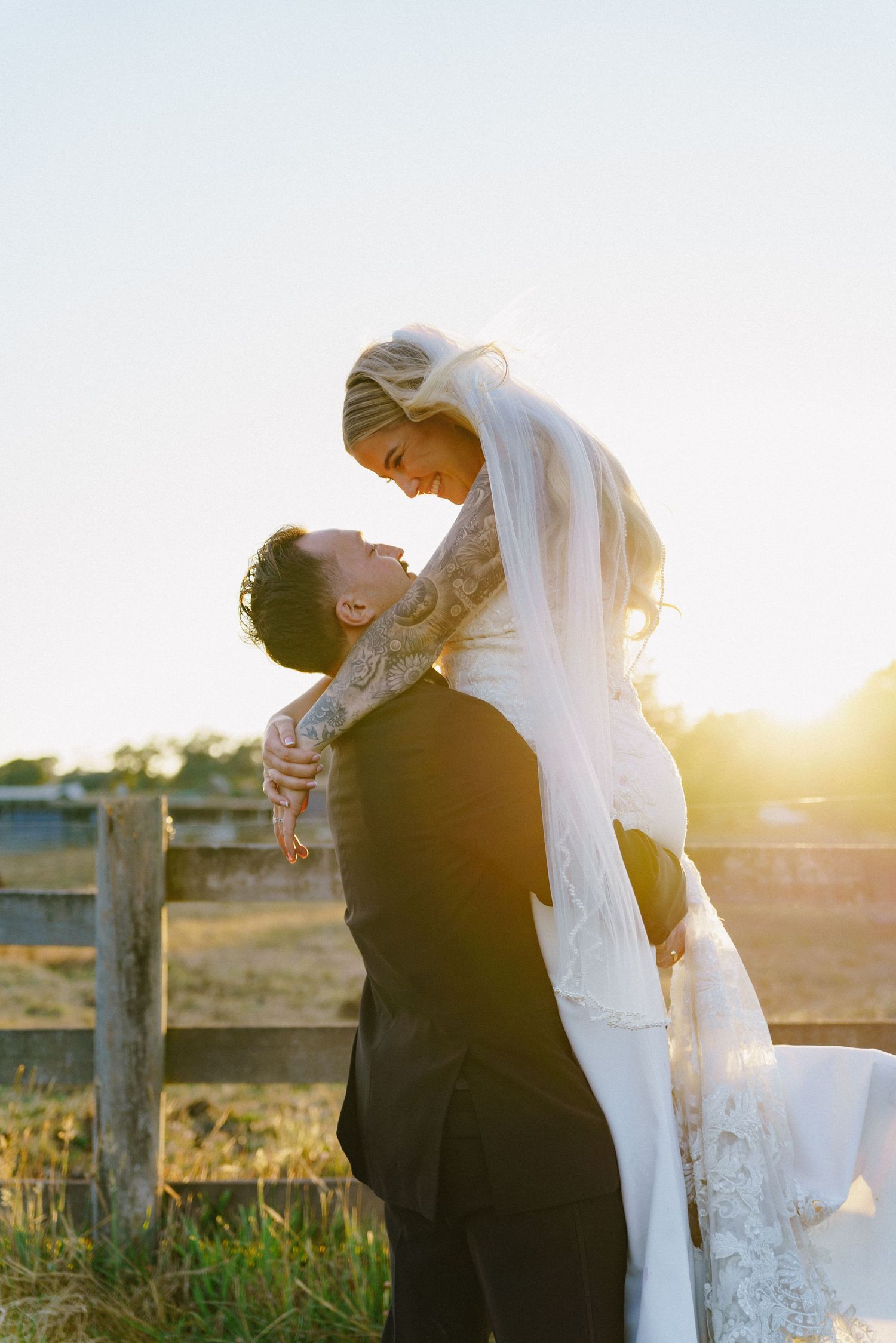 Bride and groom share tender moments during golden hour wedding photoshoot by rustic fence.