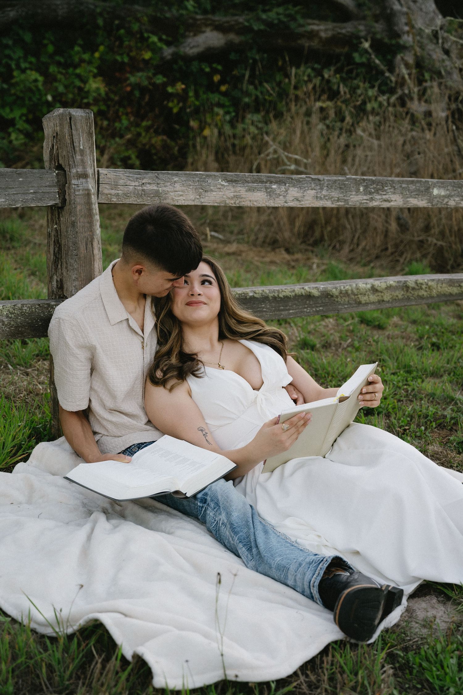 A couple relaxing on a white blanket in a grassy outdoor setting.