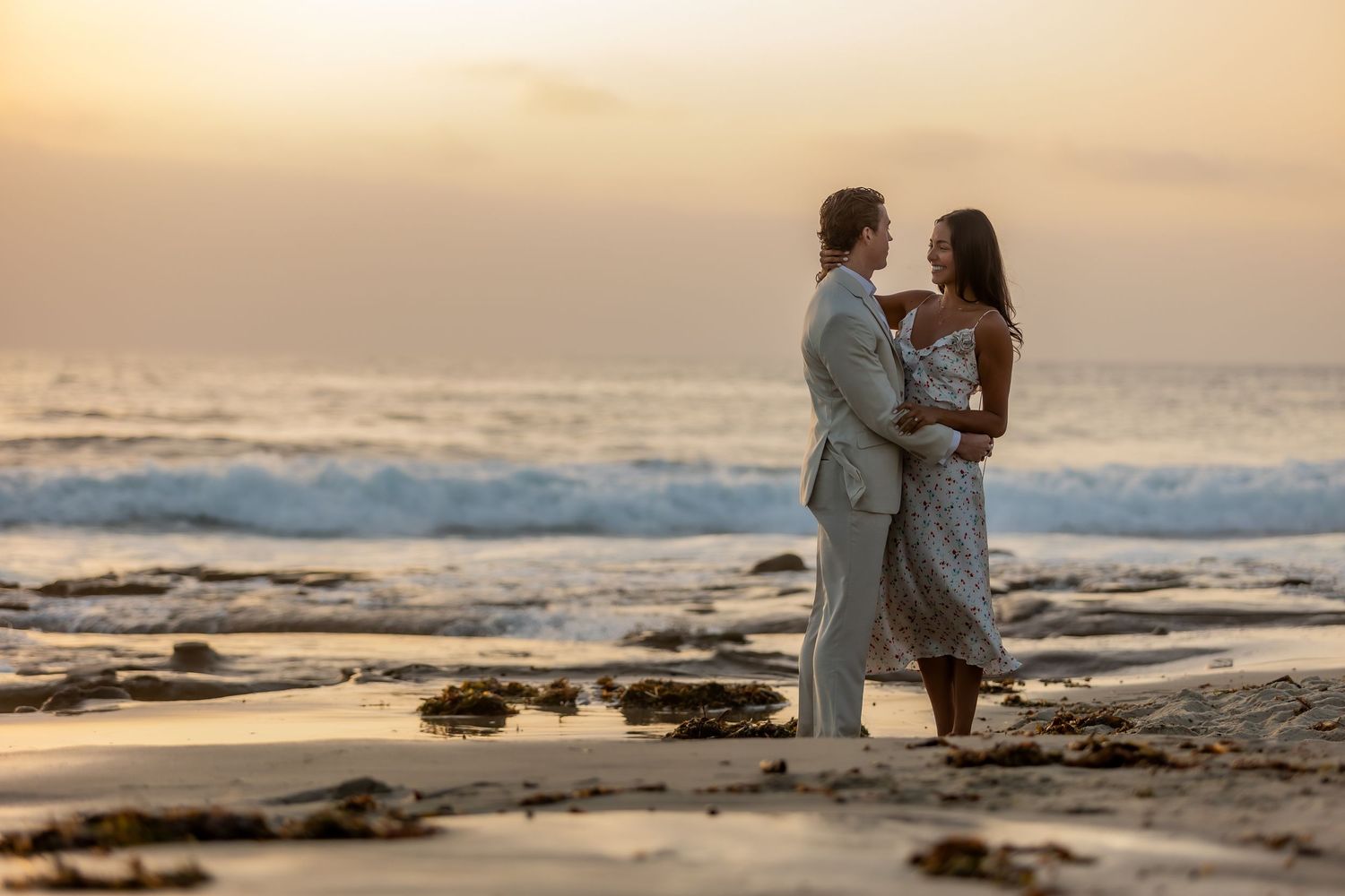 Silhouetted couple sharing an intimate moment on rocky beach during golden hour.