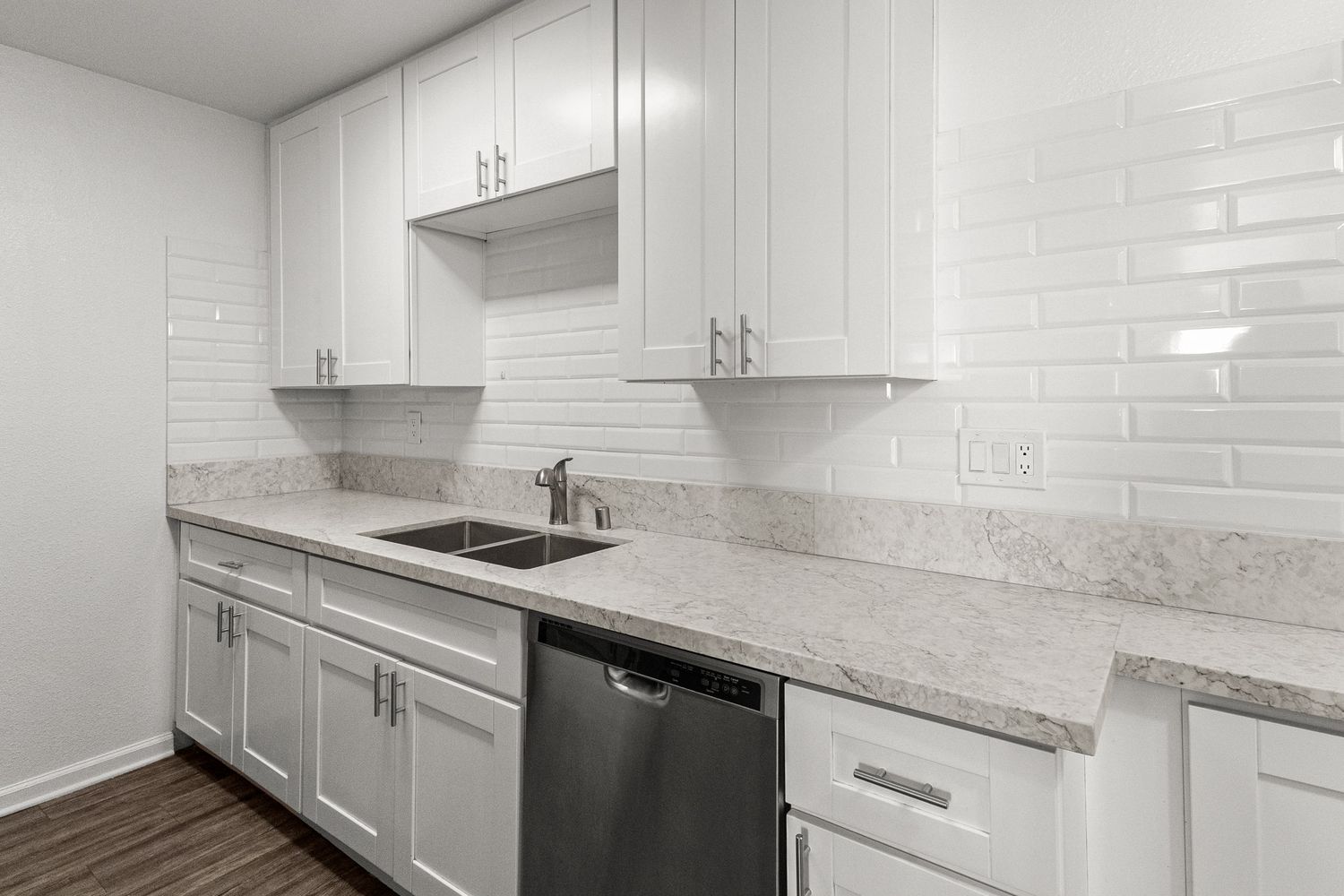 Modern white kitchen with marble countertops, shaker cabinets, and stainless steel appliances.