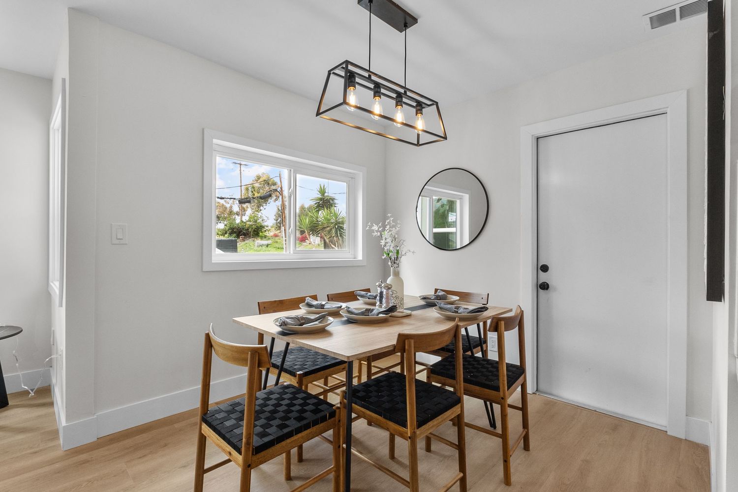 Contemporary dining area with wooden table set against bright white walls and modern light fixture.