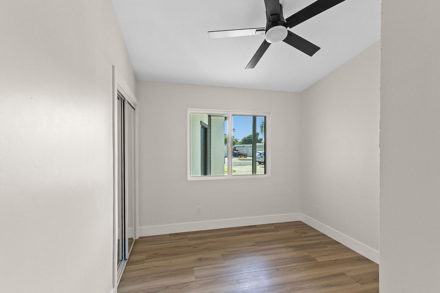 Empty bedroom with ceiling fan, white walls, and hardwood flooring.