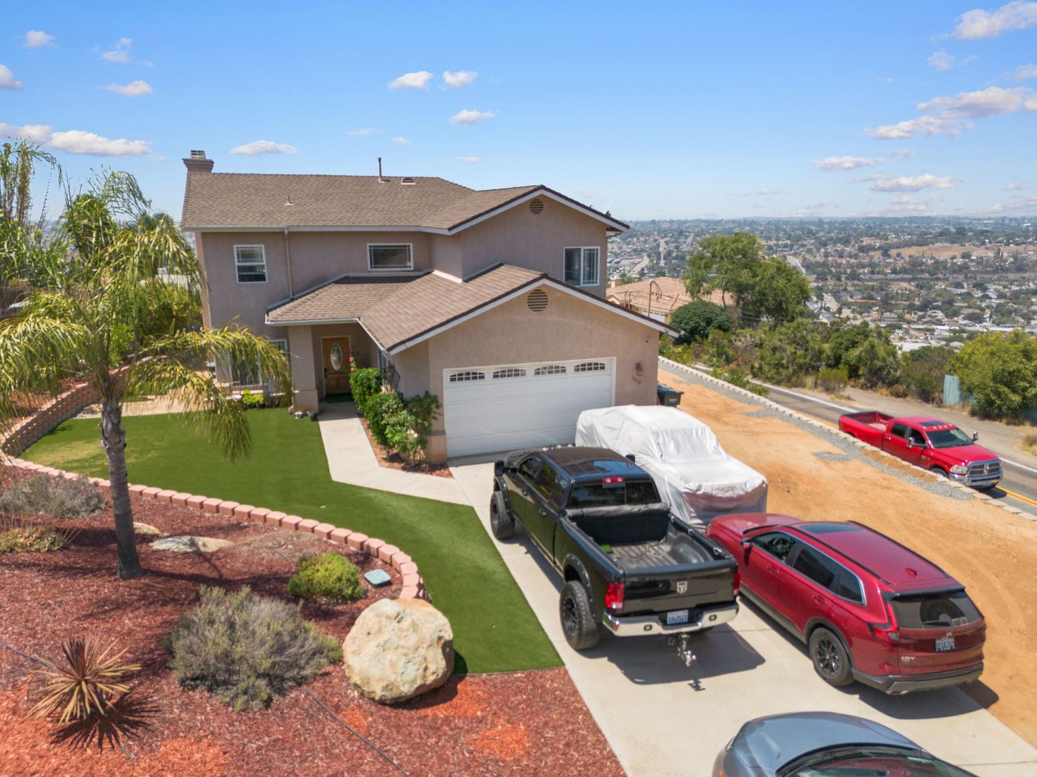 Hilltop property with cars parked in driveway offering panoramic city views.