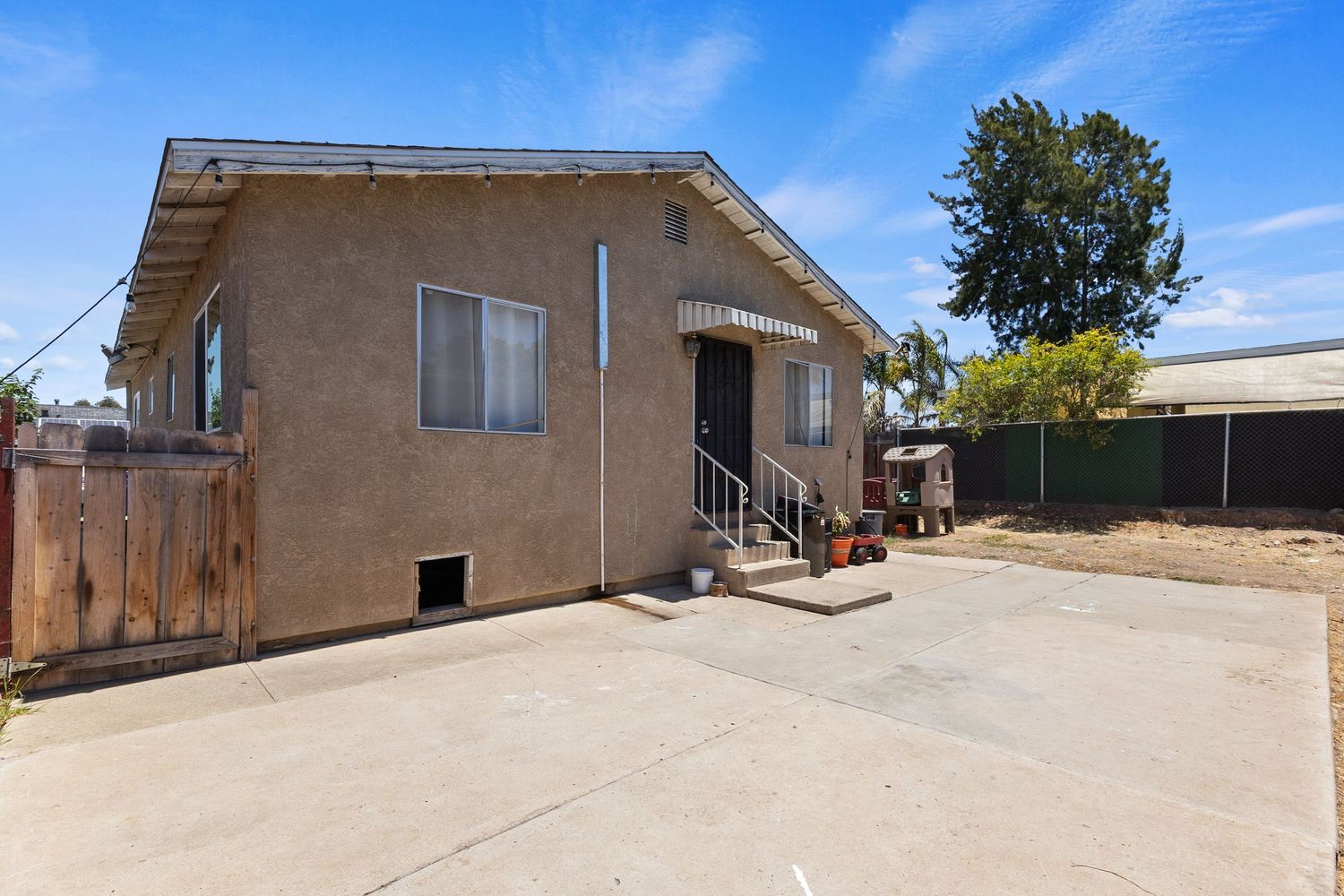 Exterior view of tan stucco house with concrete driveway under blue sky.