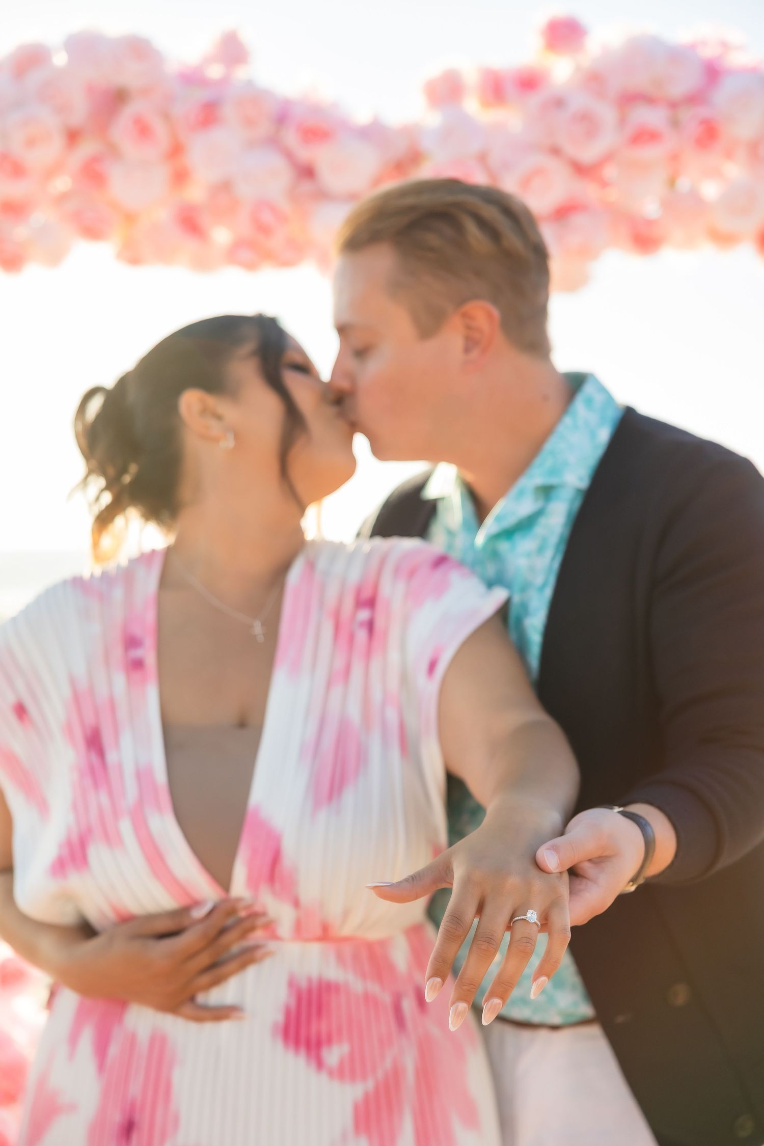 A couple embracing under pink floral decorations at sunset.