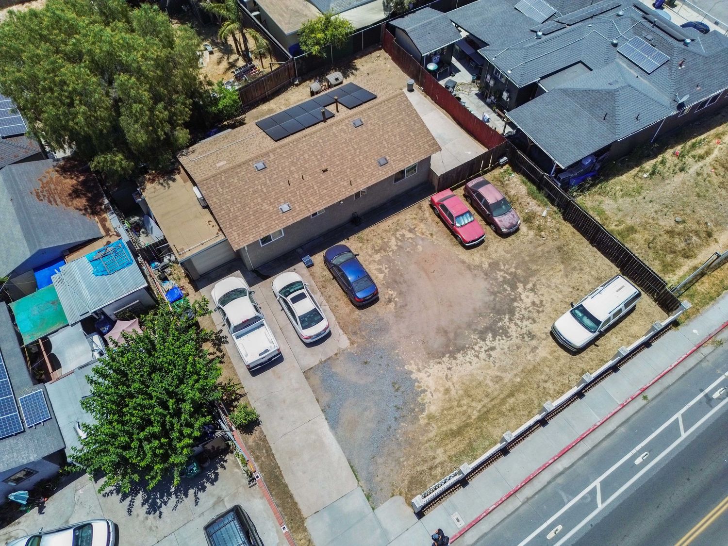 Aerial view of residential neighborhood showing multiple houses with solar panels and parked cars.