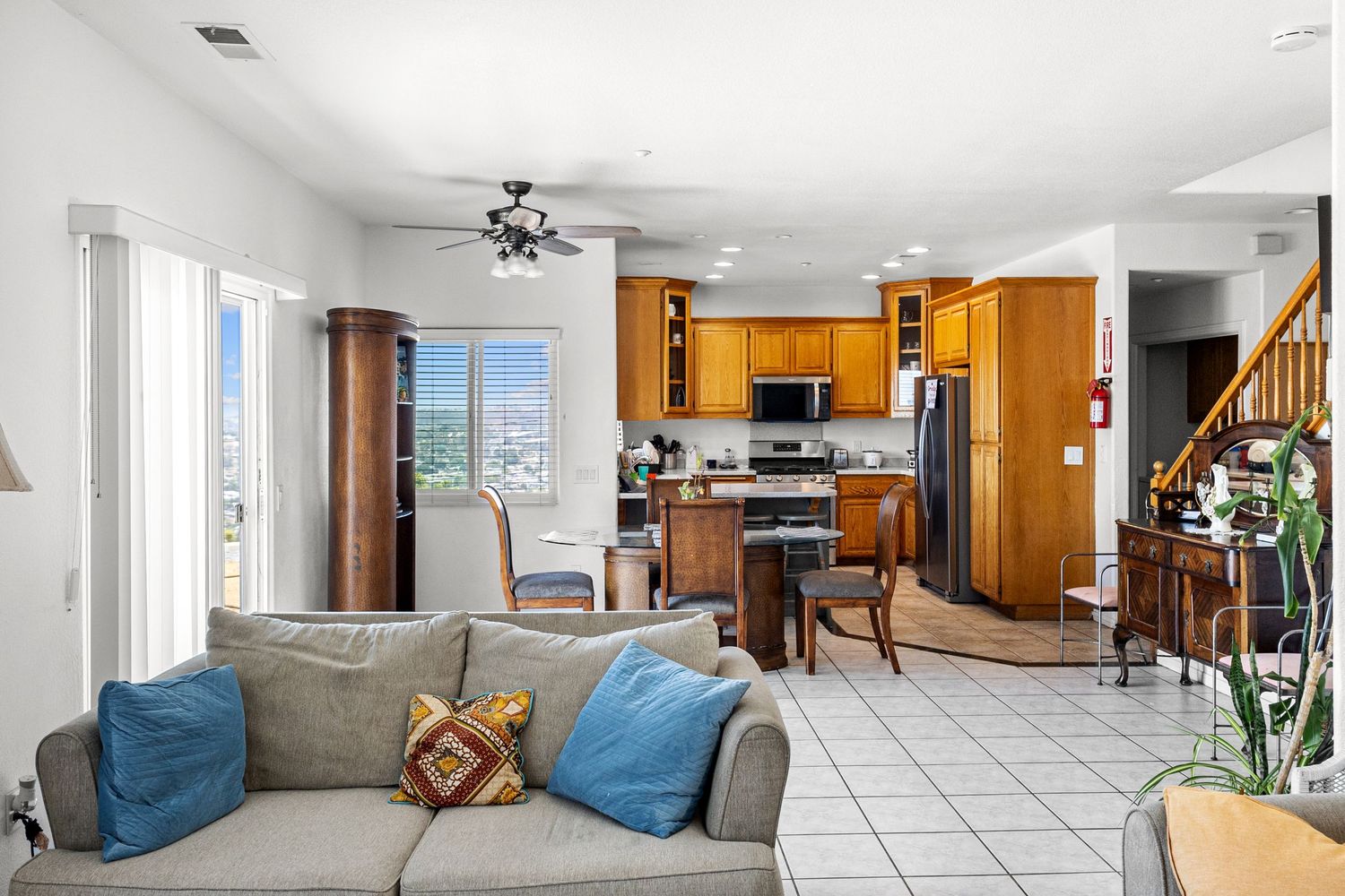 Modern open concept living room with grey sofa, blue accent pillows, and wood kitchen cabinets in background.