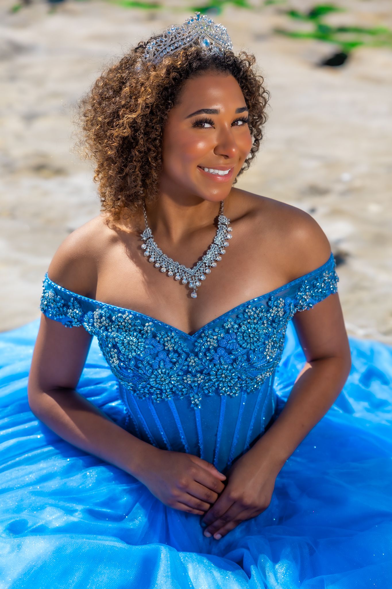Person in sparkly blue off-shoulder ball gown posing on blue fabric outdoors.