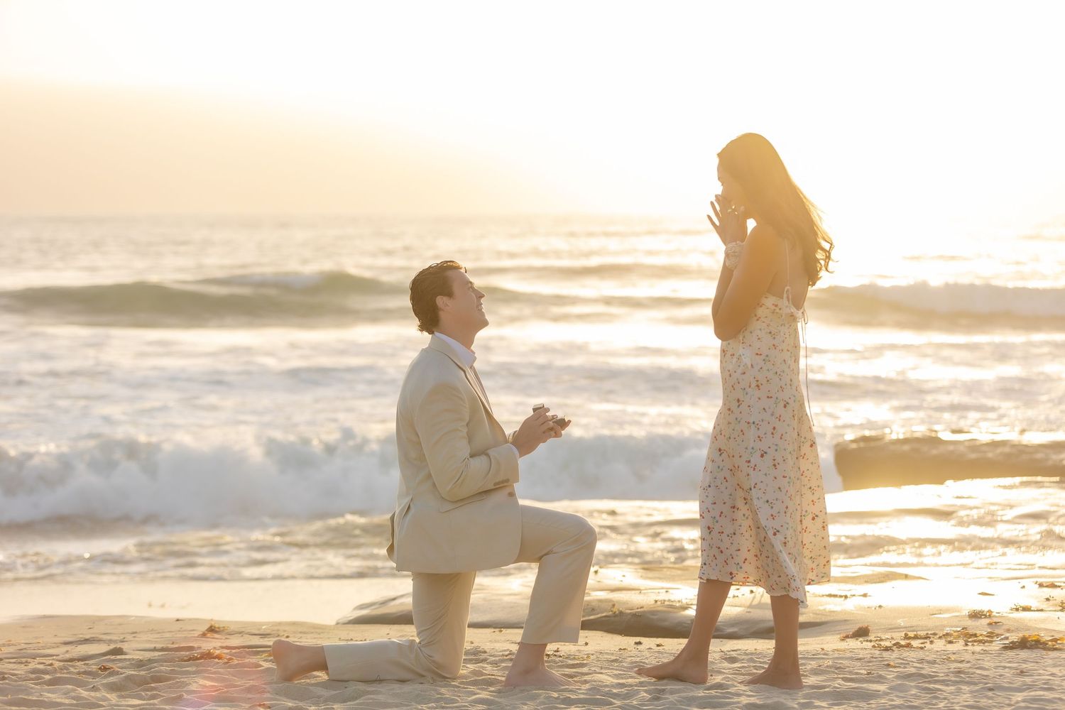 Beautiful proposal scene unfolding on beach with golden sunset light.