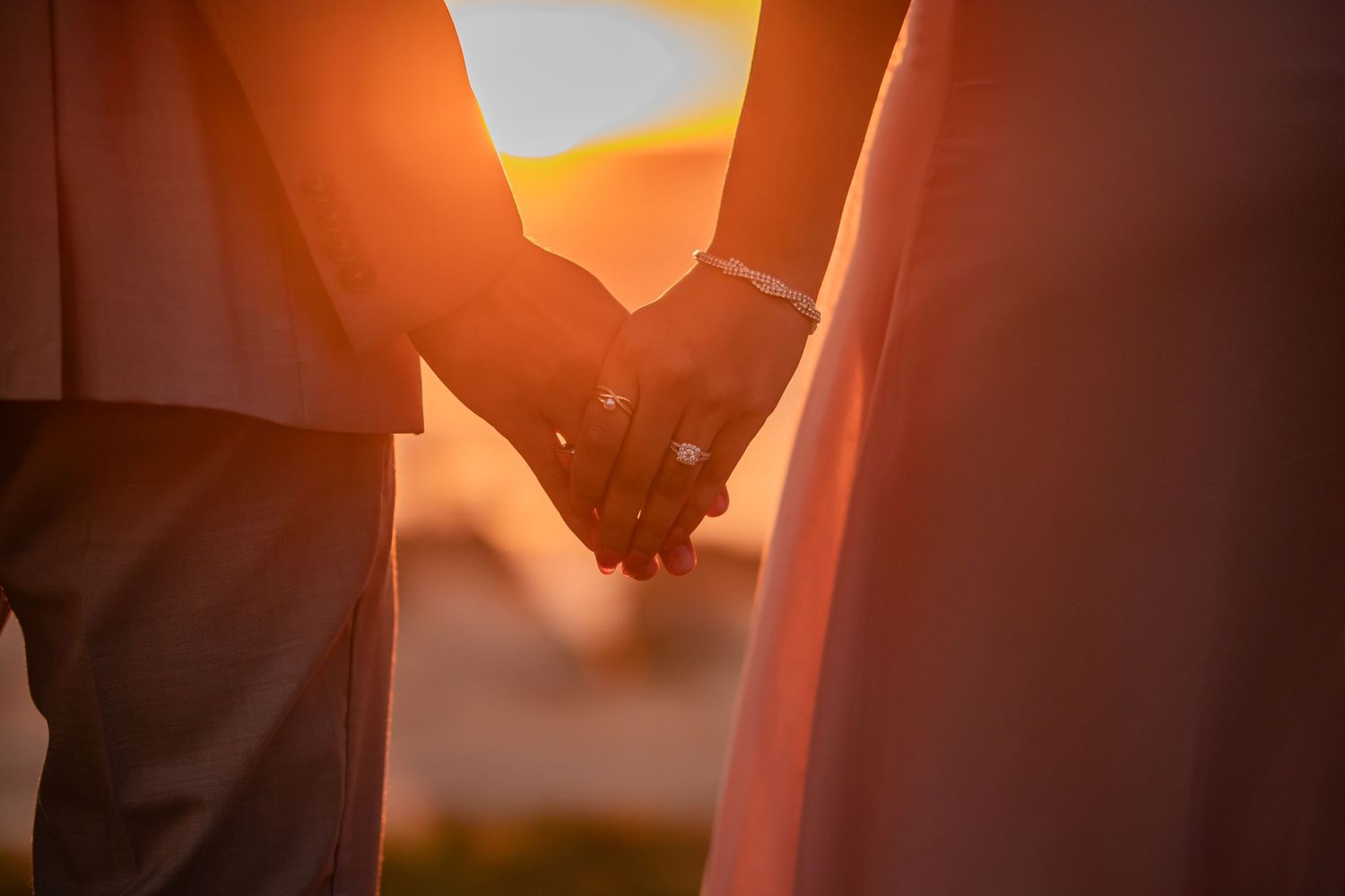 Silhouettes of couple holding hands against warm sunset backdrop.