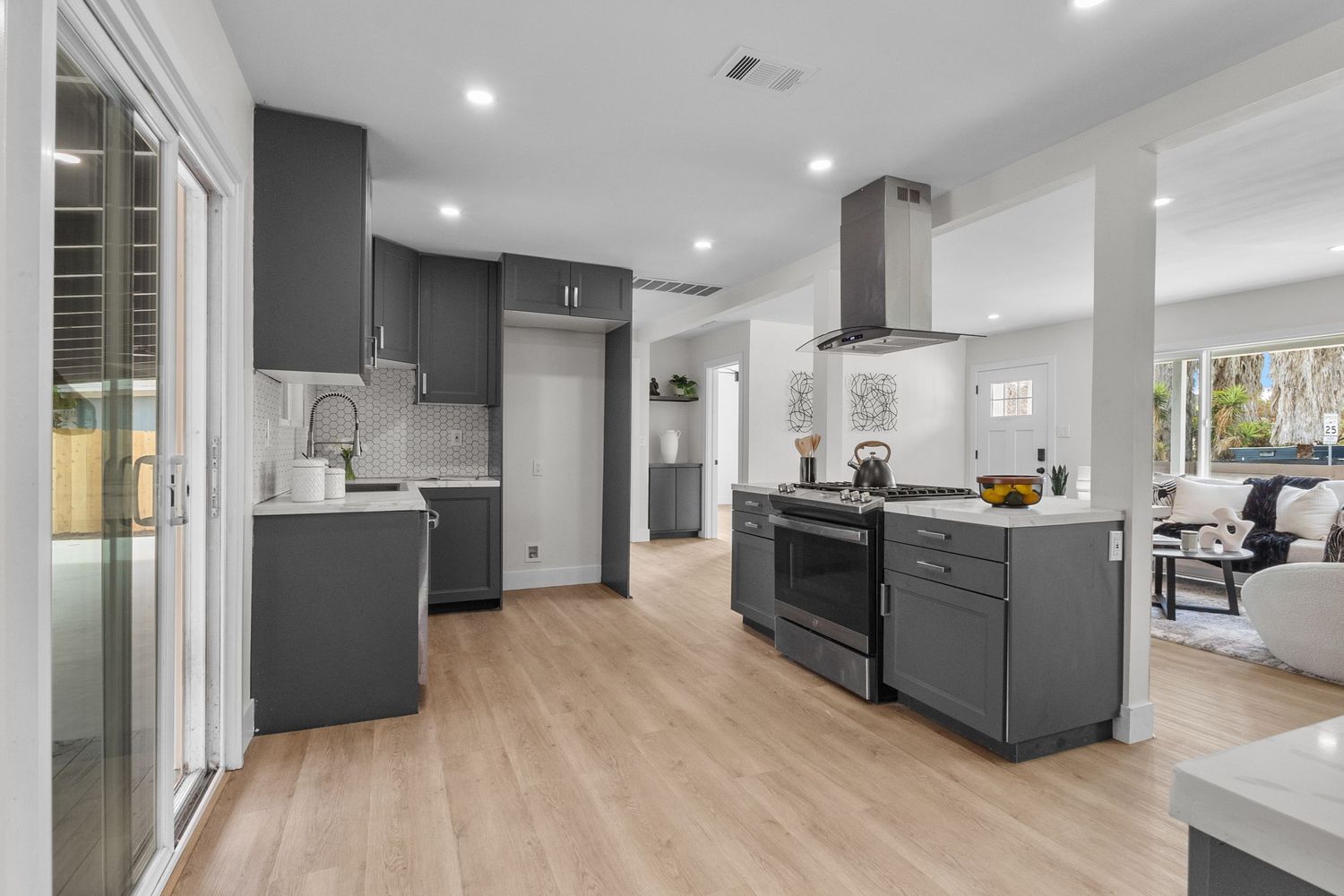 Modern open concept living space features sleek gray kitchen cabinets and white walls with recessed lighting.