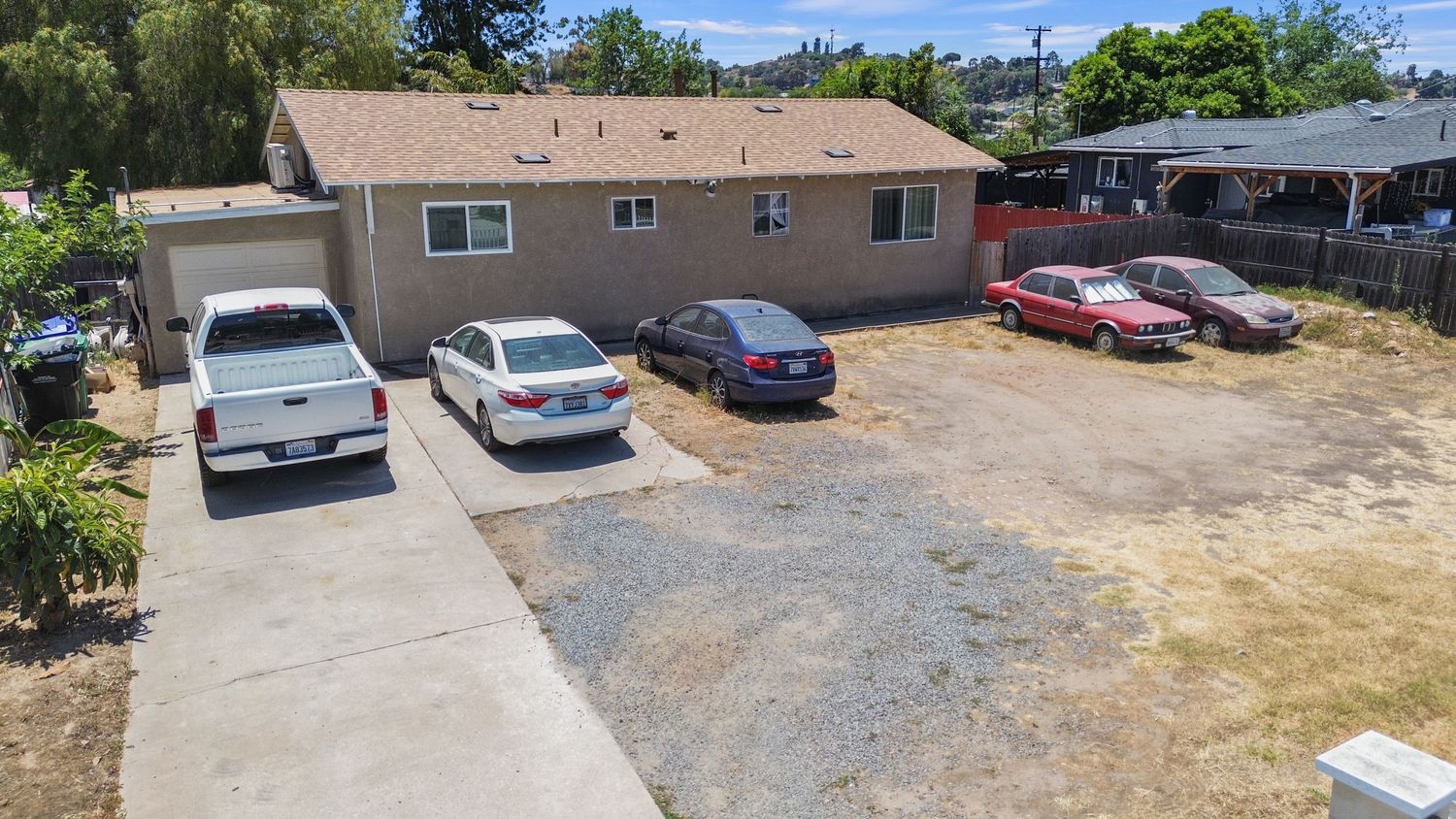 Aerial panoramic view of a residential property with parking area and surrounding greenery.