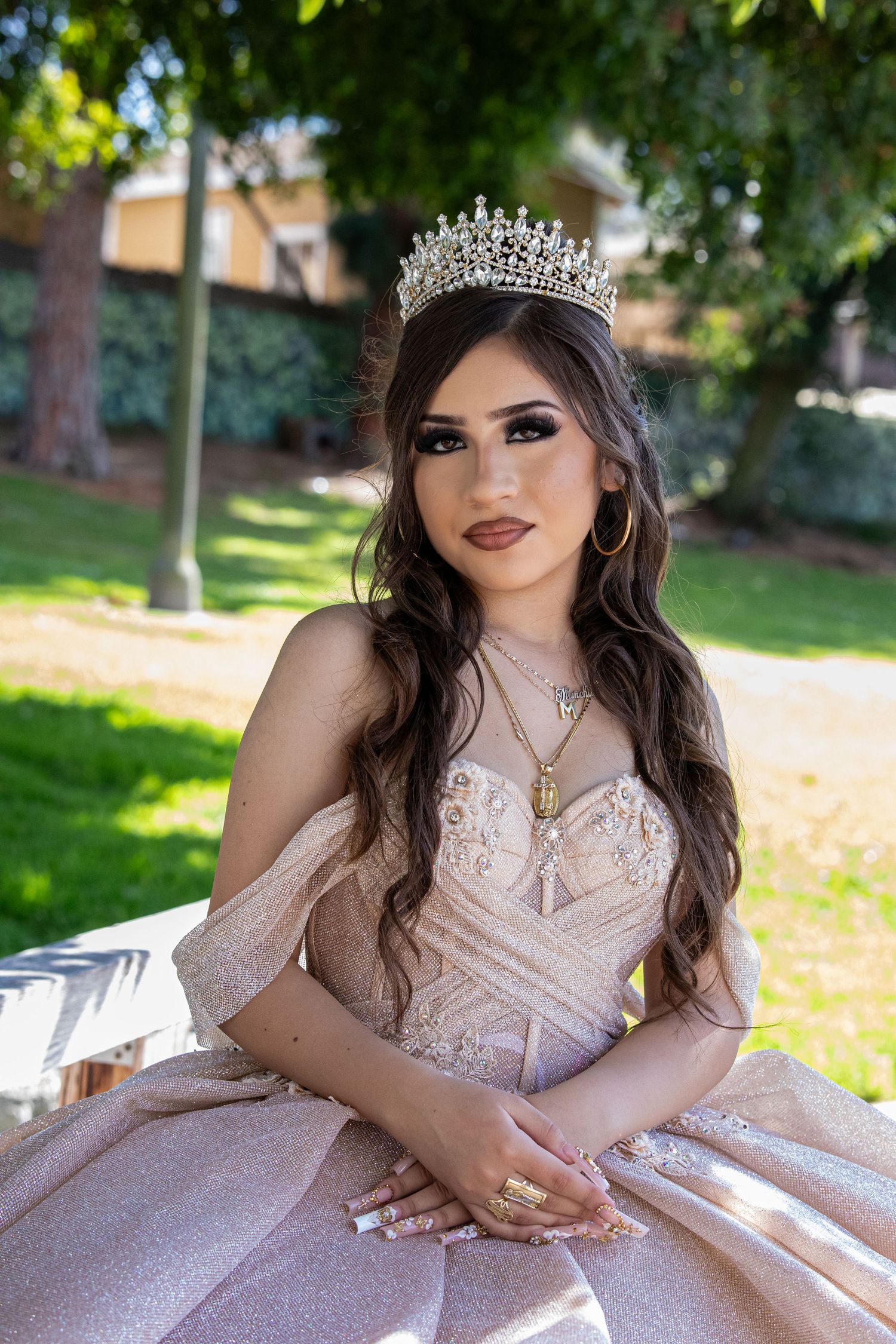 A sunlit garden portrait featuring a sparkly champagne-colored ball gown and crystal crown.