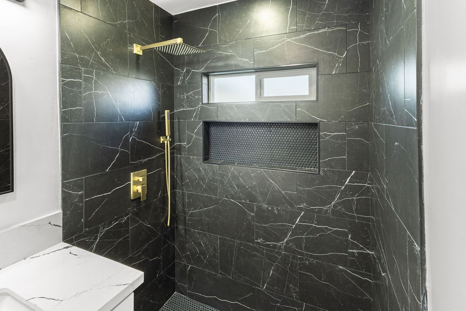 Luxurious bathroom with floor-to-ceiling black marble-effect tiles and glass shower enclosure.