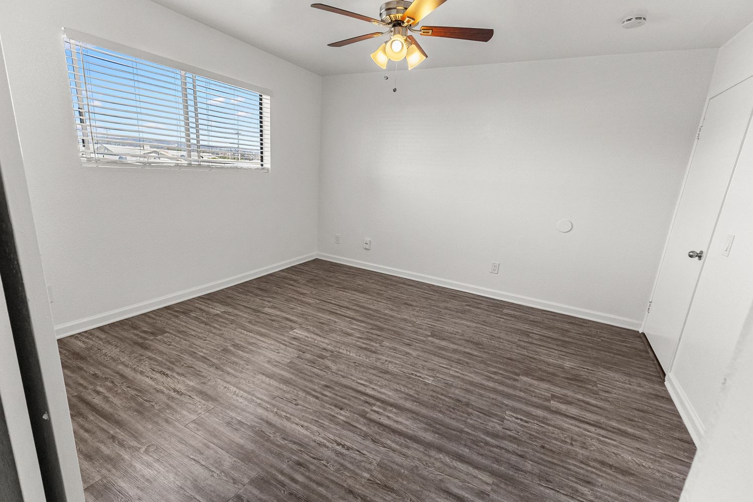 Bedroom with vinyl flooring, ceiling fan, and window letting in natural light.