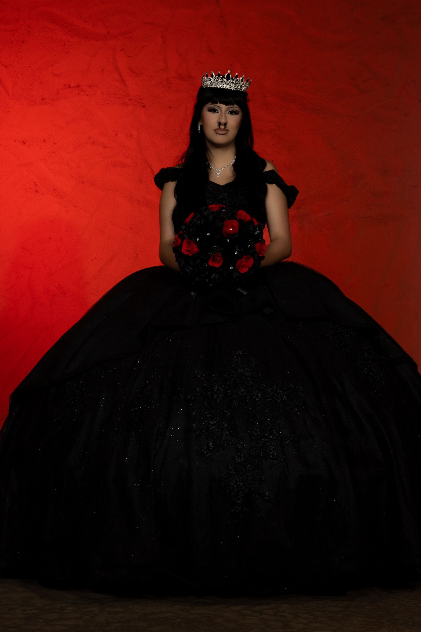 An elegant black ball gown and crown silhouetted against a vibrant red background.