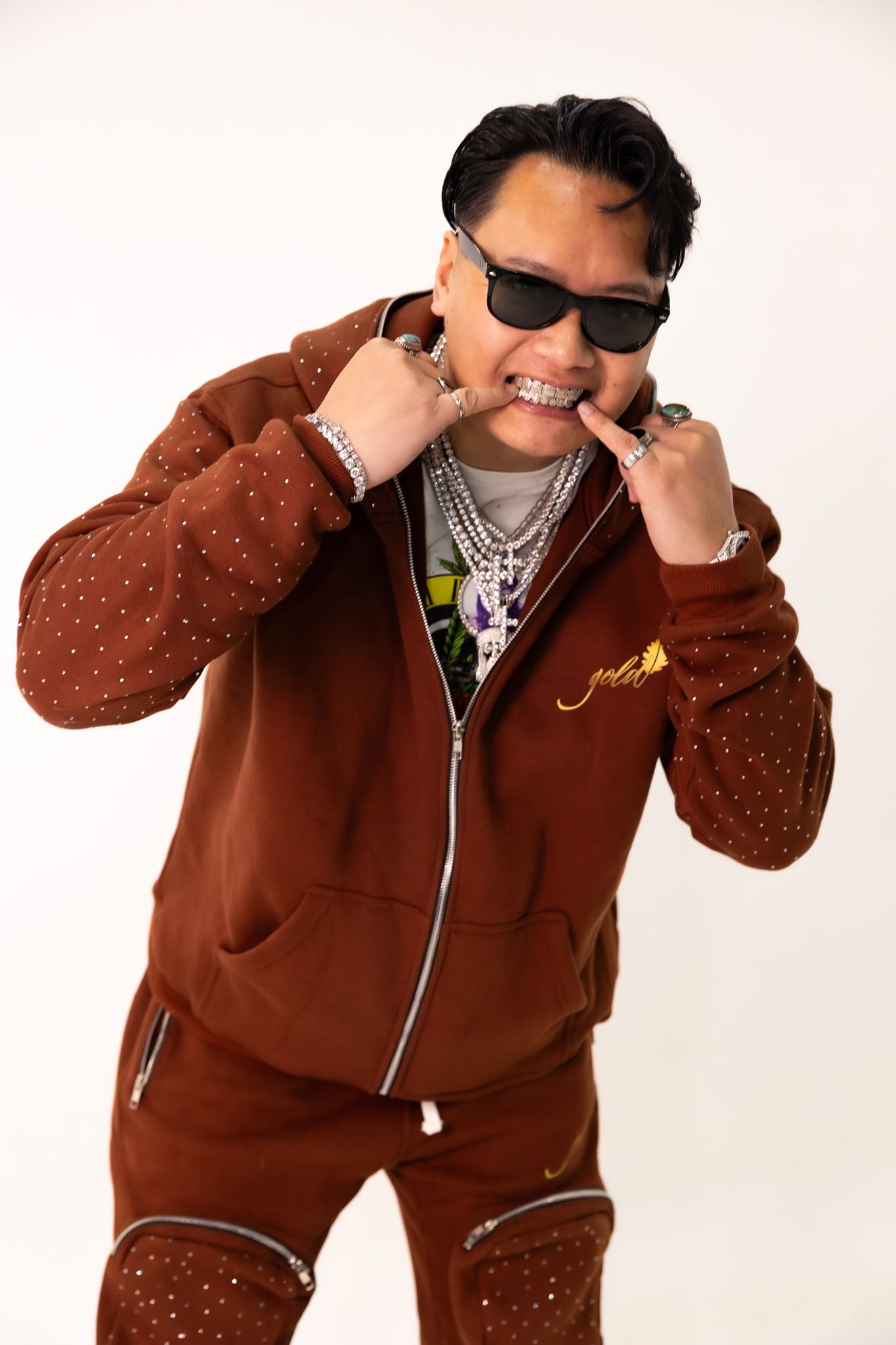 Fashion shot of model in studded brown tracksuit and sunglasses posing playfully.