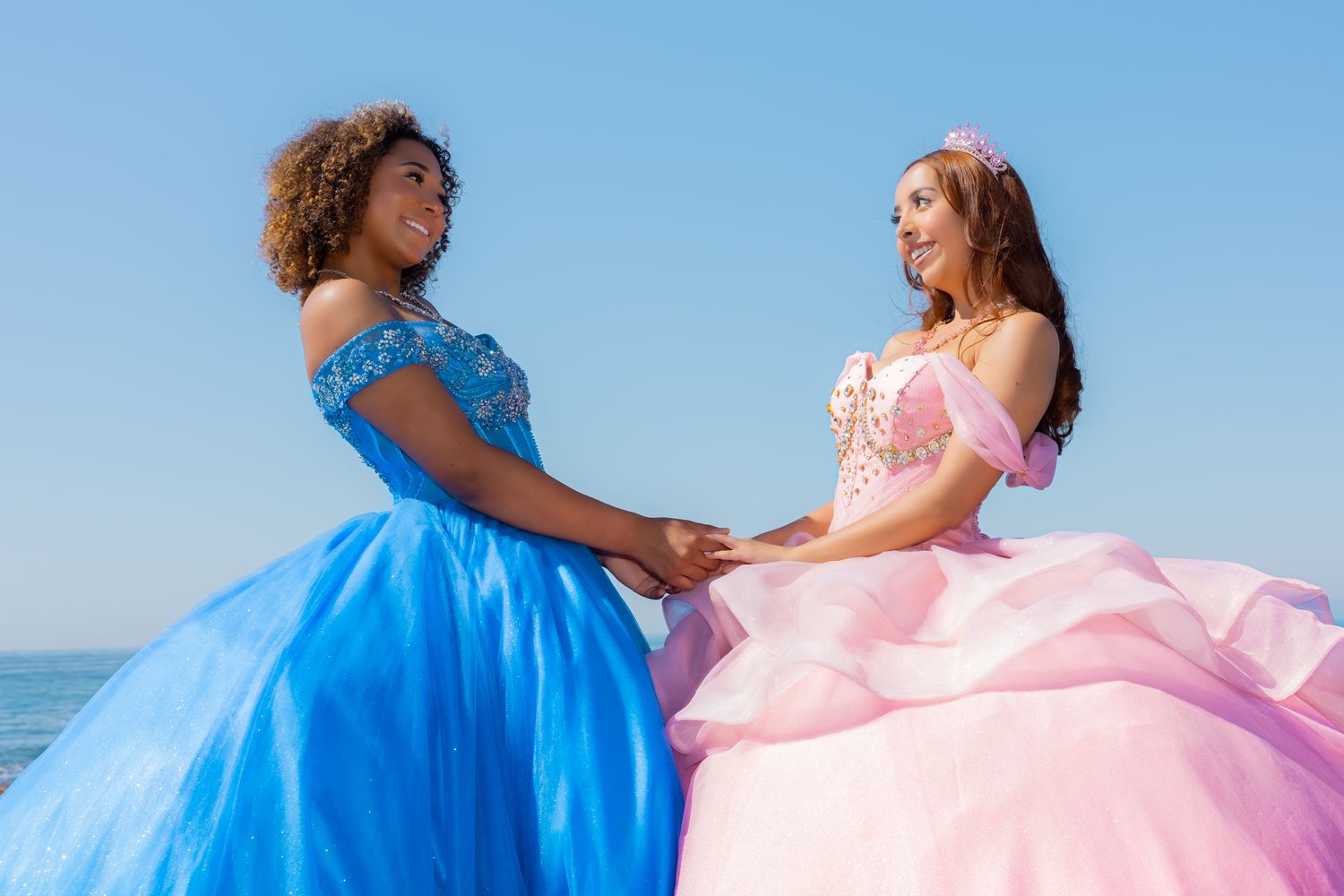 Two people in princess-style ballgowns hold hands while wearing contrasting blue and pink dresses.