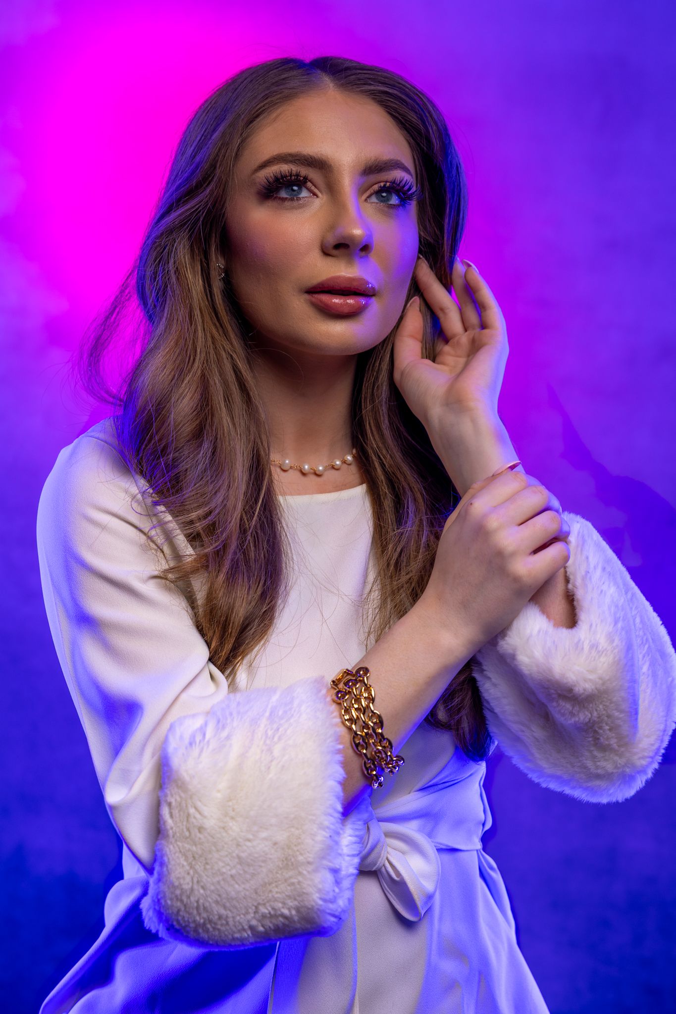 Portrait in white textured blouse with pearl necklace against neon purple and blue lighting.