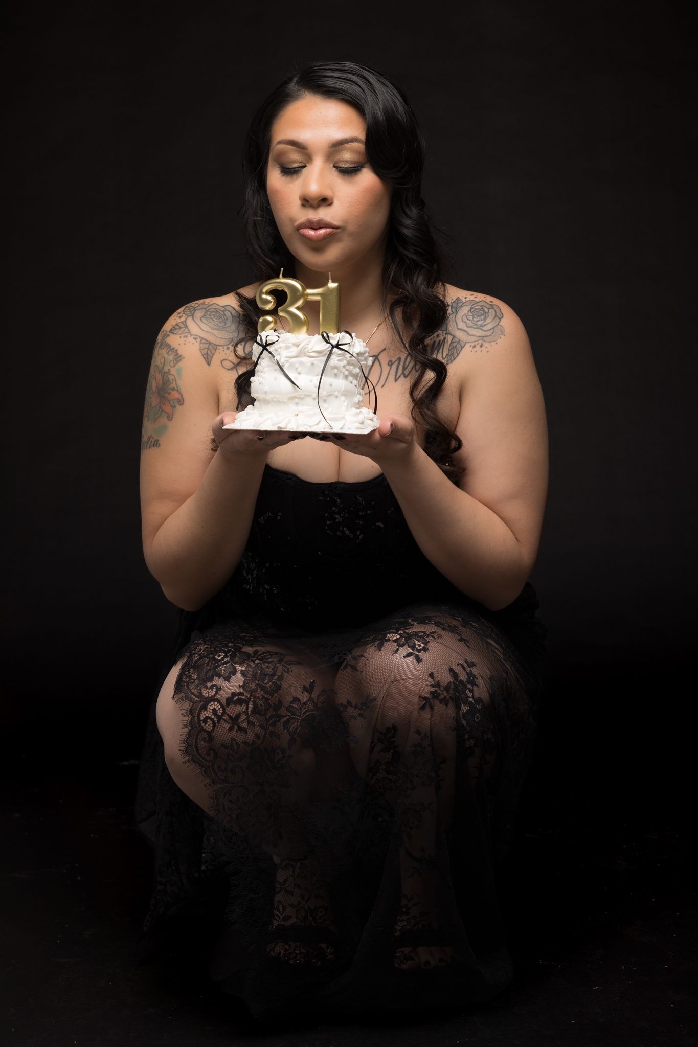 Studio portrait with subject holding and blowing out candles on a small white cake.