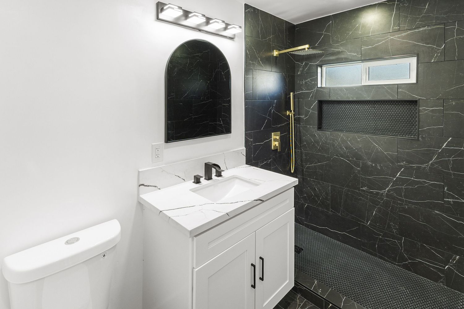 Modern bathroom featuring black marble-look walls, white fixtures, and contemporary lighting design.
