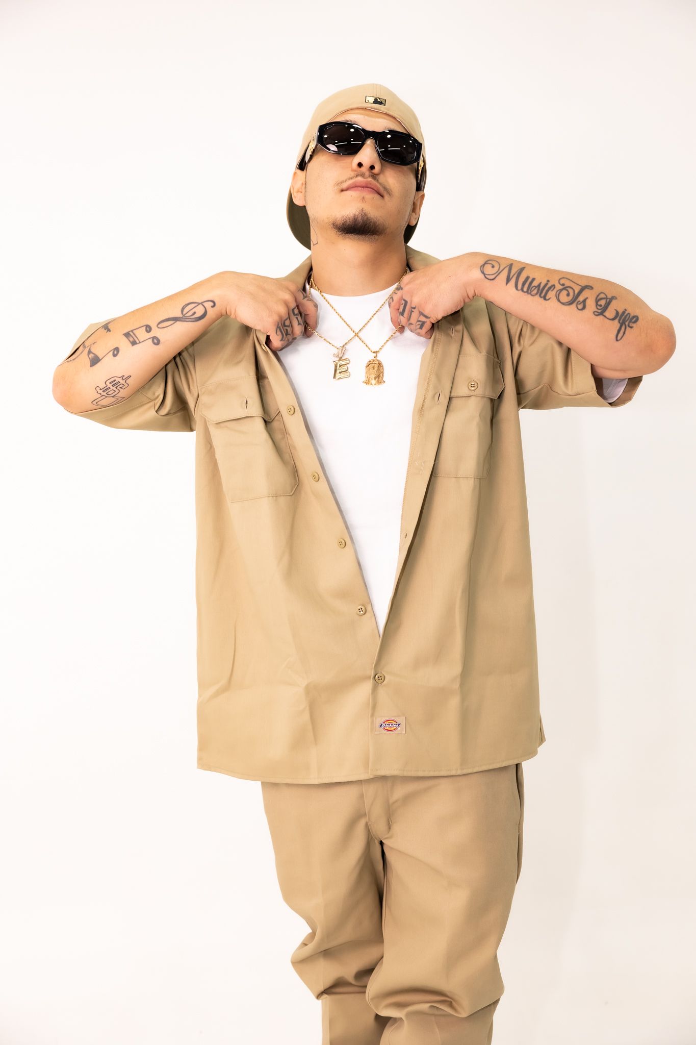 Fashion poses in beige workwear outfit showing tattoos and accessories.