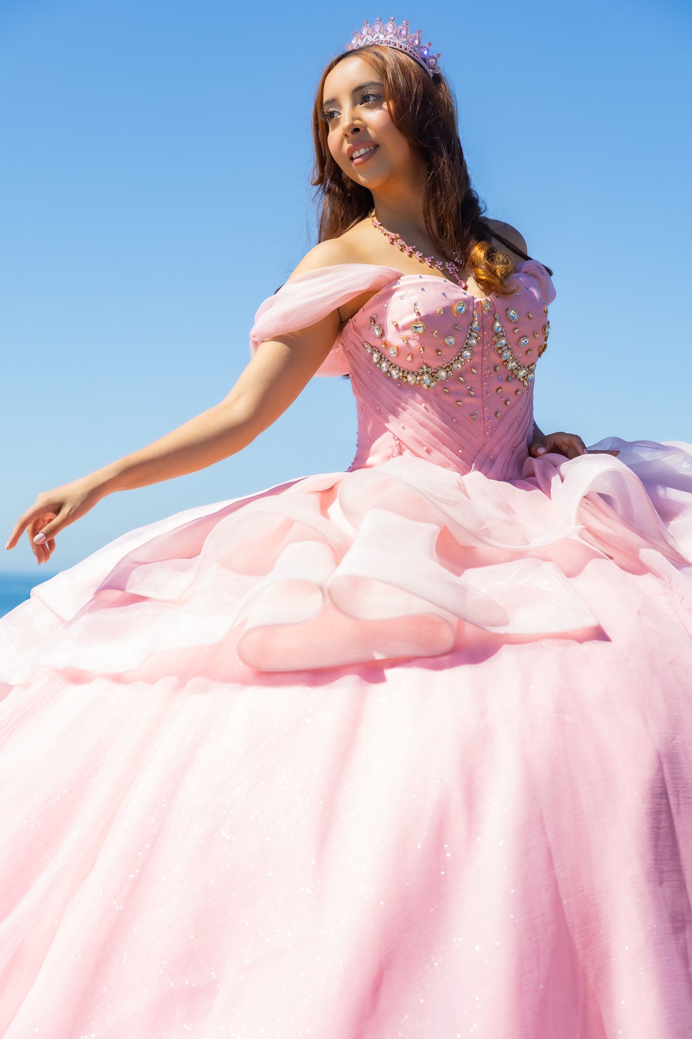 A pink princess ballgown with crystal details sparkles in the sunlight during an outdoor photoshoot.