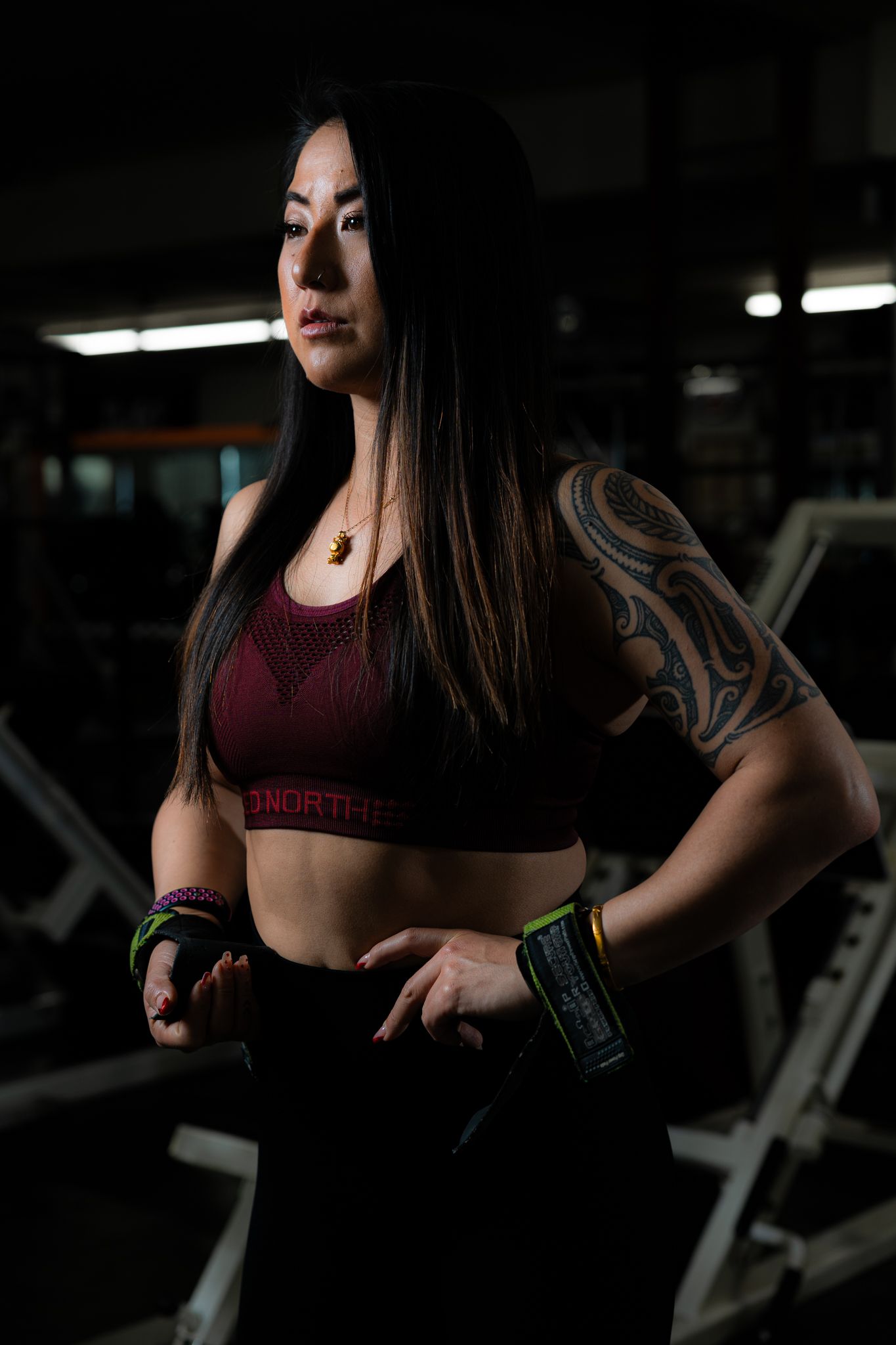 Fitness model in burgundy workout attire poses in dimly lit gym setting.