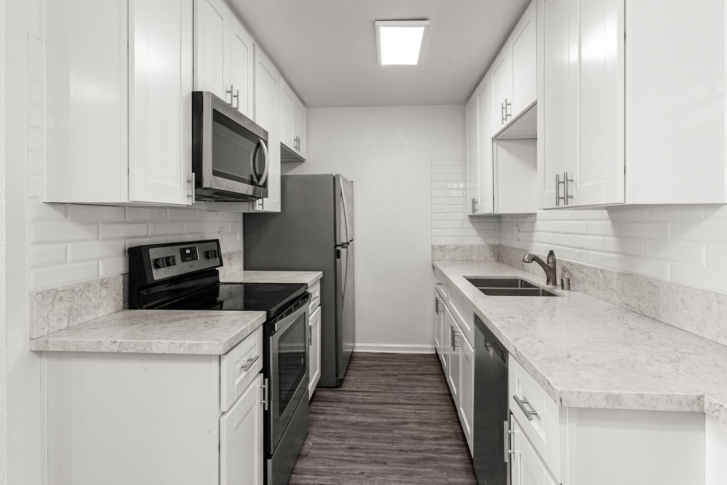 Contemporary white kitchen with marble-look countertops and stainless steel appliances.