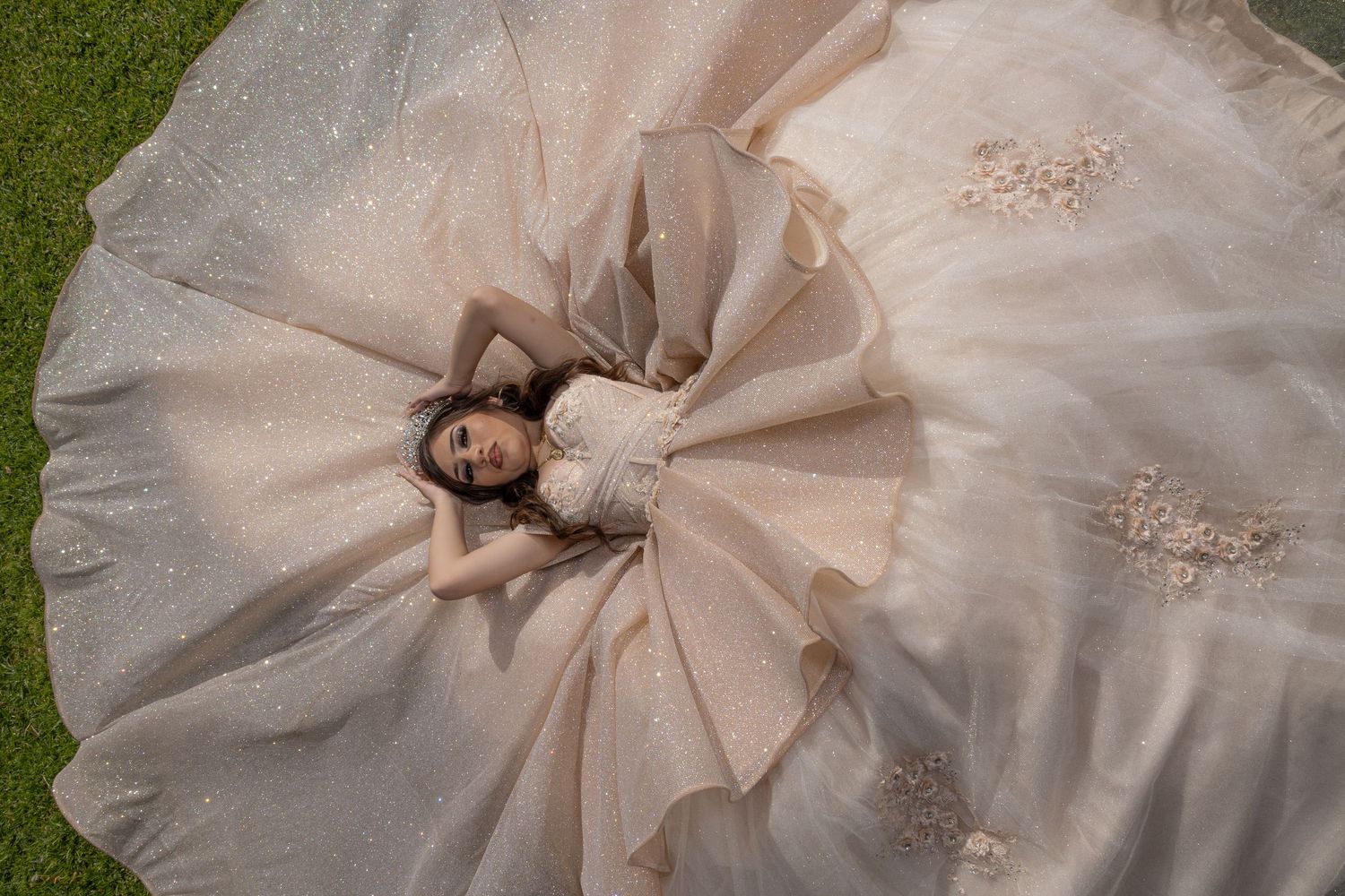 Aerial view of a champagne-colored ball gown spread in a perfect circle on green grass.